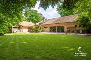 <p><strong>Riante energiezuinige villa met binnenzwembad en maximale privacy</strong></p>
<p>Op zoek naar luxe, ruimte en rust? Deze exclusieve villa, gelegen op een residentieel en rustig perceel van 2.477 m², biedt het allemaal. Met een bewoonbare oppervlakte van maar liefst 540 m² geniet je hier van comfortabel en energiezuinig wonen in een groene, discrete omgeving.</p>
<p>De woning werd gebouwd in 2006 en is voorzien van alle hedendaagse comfort. De ruime woonkamer met open leefkeuken baadt in natuurlijk licht en vormt het hart van het huis. De gehele gelijkvloerse verdieping is voorzien van gepantserd glas. Verder beschikt de villa over 5 volwaardige slaapkamers en 4 badkamers – ideaal voor grotere gezinnen of wie graag gasten ontvangt.</p>
<p>Voor ontspanning hoef je de deur niet uit: het luxe binnenzwembad zorgt voor een permanent vakantiegevoel. Ook thuiswerken wordt een plezier dankzij de grote kantoorruimte. Bovendien is er een aparte studio, perfect als gastenverblijf, praktijkruimte of voor inwonende hulp.</p>
<p>Buiten geniet je van een overdekt terras en een prachtig aangelegde tuin die volledige privacy garandeert. De dubbele garage maakt het plaatje compleet.</p>
<p>Bij het betreden van deze riante en energiezuinige villa komt u via de inkomhal meteen in de ruime leefruimte terecht. De woonkamer met gezellige zithoek en gashaard vloeit naadloos over in de eetplaats en de open leefkeuken, die voorzien is van alle hedendaags comfort – een ideale plek voor wie graag kookt en gasten ontvangt.</p>
<p>Een stijlvolle glazen wand scheidt de woonkamer van het binnenzwembad. Hoewel het zwembad momenteel buiten gebruik is, zijn alle technieken aanwezig om dit eenvoudig opnieuw in werking te stellen. Momenteel wordt de ruimte gebruikt als fitnessruimte, maar ze biedt ook andere mogelijkheden zoals wellness of hobbyruimte. Aansluitend bevinden zich een technische ruimte en een welnessgedeelte met sauna, douche en toilet. Een trap leidt hier naar een grote polyvalente ruimte op de verdieping, uitgerust met airconditioning en momenteel ingericht als kantoor.</p>
<p>Op het gelijkvloers is ook een ruime dubbele garage met toegang tot de kelder. Tussen de keuken en garage bevindt zich een tweede trap die leidt naar een studio, bestaande uit twee slaapkamers en een badkamer met douche, lavabo en toilet – ideaal als gastenverblijf of voor inwonende hulp.<br /><br />Vanuit de centrale inkomhal vertrekt een derde trap naar de bovenverdieping, waar u de masterbedroom vindt, uitgerust met parketvloer, airconditioning en gashaard. De master beschikt over een aanpalende dressing en een eigen badkamer met bad, douche en toilet. Daarnaast zijn er nog twee extra slaapkamers met parket en een aparte badkamer met ligbad, lavabo en toilet. Een gastentoilet is eveneens voorzien op het gelijkvloers.</p>
<p><strong>Buitenleven in alle comfort</strong></p>
<p>Grenzend aan de woonkamer bevindt zich een ruim overdekt terras, uitgerust met elektrische rolschermen en terrasverwarming – ideaal om het hele jaar door van buiten te genieten. Een tweede terras ligt aan het binnenzwembad. De aangelegde tuin rondom de woning biedt volledige privacy en rust. Verder beschikt het domein over een carport en een professioneel alarmsysteem.</p>
<p>Een unieke combinatie van ruimte, luxe en rust. Klaar om jouw nieuwe thuis te worden?</p>