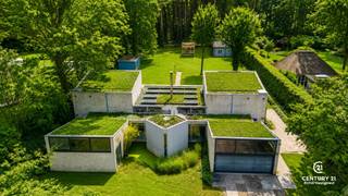<p><strong>Unieke villa onder architectuur van Lou Jansen op royaal perceel van +3.000 m² in villawijk “De Lint”</strong></p>
<p>Op een prachtig zuidgericht perceel van meer dan 3.000 m², in de gewaardeerde villawijk <em>De Lint</em> en op wandelafstand van natuurgebied De Liereman, bevindt zich deze bijzondere woning die volledig onder architectuur van Lou Jansen (Turnhoutse School) werd ontworpen. De ligging is bovendien uitstekend: op slechts ca. 25 minuten rijden van zowel Eindhoven als Antwerpen.</p>
<p>De woning is volledig te renoveren, maar biedt dankzij haar uitzonderlijke bewoonbare oppervlakte van 334 m² en veelzijdige indeling een zee aan mogelijkheden. Verschillende binnenmuren zijn verplaatsbaar, waardoor u de ruimtes volledig naar wens kunt herinrichten.</p>
<p>De huidige indeling omvat een ruime, lichte woonkamer en een keuken die beide uitkijken op de prachtige achtertuin en het zonovergoten terras — een echte kers op de taart. Op het gelijkvloers bevindt zich bovendien een slaapkamer met ensuite badkamer en directe toegang tot de tuin. Aan de voorzijde is een bureauruimte voorzien die desgewenst als extra slaapkamer kan dienen.</p>
<p>Aan zowel de linker- als rechterzijde van de woning leidt een trap naar de bovenverdieping. Elke zijde beschikt over twee slaapkamers en een gedeelde badkamer, ideaal voor een grotere familie of logeerfunctie.</p>
<p>De inpandige garage biedt plaats aan twee wagens. In de volledig zuidgeoriënteerde tuin staan daarnaast enkele charmante chalets in goede staat, geschikt als bergruimte, atelier of hobbyruimte.</p>
<p><strong>Kortom, dit is een uniek renovatieproject waarbij u de kans krijgt om een architecturaal waardevolle woning volledig naar uw hand te zetten — een echte parel op een uitzonderlijke locatie.</strong></p>