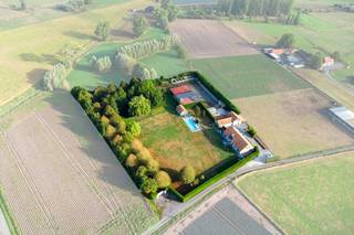 Tussen het groen in Zwevezele, op een riant domein van 10.997 m², biedt deze instapklare eigendom uit 2006 een uitzonderlijk totaalpakket voor wie riant wil wonen én professioneel wil ondernemen. De locatie garandeert rust en privacy, gecombineerd met een vlotte aansluiting richting Torhout, Roeselare en de E403. <br /><br />Het huis verrast door een indrukwekkende lichtinval, doordachte ruimtes en een hoogwaardige afwerking. Het gelijkvloers omvat een royale leefruimte met sfeervolle haard, een volledig uitgeruste leefkeuken met bijkeuken en koelcel, een bureau, drie slaapkamers en een ruime badkamer. Boven bevindt zich een extra woongedeelte — voorzien van een leefruimte, keuken, zonneterras, badkamer, dressing en twee extra slaapkamers. Deze indeling leent zich ideaal voor kangoeroewonen, een gastenverblijf of een praktijk.<br /><br />Buiten treft u een hoogwaardig aangelegde tuin waar rust en privacy centraal staan. Het uitnodigende zwembad, de jacuzzi en de sfeervolle vijver vormen samen het hart van het domein, met op de achtergrond een prachtig, vrij uitzicht over de omliggende velden. Het  bijgebouw — compleet ingericht met een sauna en inloopdouche — tilt het comfort op eigen terrein naar een nog hoger niveau. Een heerlijke plek om in volledige discretie te ontspannen en van het buitenleven te genieten.<br /><br />Voor zelfstandigen of ondernemers zijn de logistieke voorzieningen ongewoon uitgebreid op eigen terrein: een ruime hoofdloods, een tweede loods met dubbele doorrijpoort, overdekte opslagruimtes, een dubbele garage en drie garageboxen. Bovendien is de eigendom toekomstgericht uitgerust met een milieuvriendelijke warmtepomp, 58 zonnepanelen en 60.000 liter regenwateropslag.<br /><br />Bestuursmaatregelen in het maatregelenregister: nee