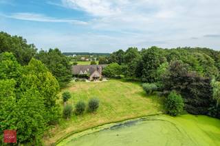 Prachtige eigendom met bos, prachtige tuin, vijver en ruim landhuis bestaande uit inkomhal, bureel, zeer ruime living met open haard, eetplaats, keuken met ontbijthoek en koelcel, wasplaats, kelders en een ruim overdekt zwembad (of hobbyruimte) met jacuzzi, verkleedruimte en douche. Ruime slaapkamer met badkamer en dressing op gelijkvloers en 2 ruime kamers (ev. 3) met badkamer op verdiep. Garage met zolder (hobbyruimte), tuinberging, en ruime terrassen met zicht op landschapstuin met vijver.<br />Eventueel mogelijk ca. 4.700m² landbouwgrond bij te kopen.<br /><br />