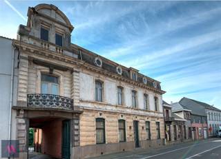 Deze neoclassicistische herenwoning anno 1868 met dubbelhuisopstand, de voormalige brouwerswoning van de brouwerij Du Bois-Haems, is gelegen in hartje Lebbeke, temidden van de driehoek Brussel-Gent-Antwerpen. Het interieur bevat talloze decoratieve elementen, waaronder een salon in Lodewijk XVI-stijl, mozaïekvloeren, stucplafonds, marmeren schouwen,...Dit pareltje heeft een parktuin van 59 are 51 ca met vijver, Lourdesgrot, antiek zwembad en talrijke imposante bomen waaronder een bruine beuk en linden. Deze indrukwekkende woning heeft een zeer ruime leefruimte (94 m²) met 3 schouwen en een leefkeuken (51 m²) met oa een AGA-fornuis, op de verdieping zijn er onder andere 7 slaapkamers en 2 badkamers. Naast de 2 garages, de wijnkelder, de paardenstallen en een gastenverblijf is er een inrijpoort met automatische poort en een met kasseien nieuw aangelegde binnenkoer. Alle technieken werden recentelijk vernieuwd (centrale verwarming op aardgas, riolering, elektriciteit), alsook de leefkeuken en de 2 badkamers met Old English douche,ligbad en wastafels. Deze woning is beschermd als monument, waardoor U kan aankopen onder het gunstig stelsel van 1% registratiekosten op voorwaarde dat de woning als gezinswoning wordt aangewend én dat er investeringen worden gedaan aan het pand. Zoniet blijft de 5%-regel gelden. Het bekomen fiscaal voordeel wordt aanzien als een fictieve subsidie, waarbij de koper binnen de vijf jaar na zijn aankoop 6% van de aankoopprijs dient te investeren in onderhouds- of renovatiewerken van het pand. Zodoende zou de nieuwe eigenaar dus 7% van de aankoopprijs betalen, zijnde 1% registratierechten en 6% aan investeringen. U kan ook daarnaast ook genieten van restauratie-en of renovatiepremies. Meer info op: https://www.onroerenderfgoed.be/nl/premies/ EPC: 432 kWh/m²/j. en UC:2070674-RES-2