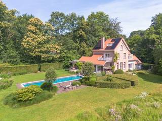 <p>In een van de meest gegeerde residentiële buurten van Brasschaat, midden in het groene Ter Borcht, bevindt zich deze karaktervolle villa op een prachtig aangelegd perceel van ca. <strong>4.850 m²</strong>. Omringd door volwassen bomen en een uitzonderlijk mooie tuin geniet u hier van absolute rust en privacy.</p>
<p>De woning, oorspronkelijk gebouwd in 1928, werd ongeveer achtien jaar geleden grondig gerenoveerd en sindsdien steeds met veel zorg onderhouden en verder gemoderniseerd. Zo werden recent nog een volledig nieuw dak, zonnepanelen en een laadpaal geplaatst.</p>
<p>Via de inkomhal met gastentoilet bereikt u het bureau, de garage en de leefruimtes. De royale woonkamer met parketvloer, open haard en gezellige zithoek baadt in het licht dankzij de grote raampartijen en biedt een prachtig uitzicht over de tuin en het zwembad.</p>
<p>De ruime leefkeuken, afgewerkt met natuursteen en voorzien van alle hedendaagse toestellen, vormt het hart van de woning en geeft rechtstreeks uit op het zonnige terras.</p>
<p>Op de eerste verdieping bevinden zich twee ruime slaapkamers, elk met een eigen badkamer. De tweede verdieping biedt nog twee bijkomende slaapkamers en een douchekamer, ideaal voor een groot gezin of gasten.</p>
<p>Buiten vormt de schitterend aangelegde tuin een ware oase van rust. Het verwarmde zwembad (14 x 4 m) met warmtepomp, de verschillende terrassen en de volwassen beplanting zorgen voor een uitzonderlijke woonbeleving in een groene omgeving.</p>