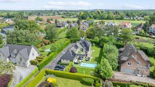 Deze exclusieve, vrijstaande villa in landelijke stijl in Wemmel straalt pure klasse uit. Met een royale bewoonbare oppervlakte van 526 m² en een superieure afwerkingsgraad geniet u hier van uitzonderlijk wooncomfort. De zandkleurige gevel combineert harmonieus met charmante dakkapellen en een monumentale glaspartij bij de inkom. De woning is energie-efficiënt uitgerust met zonnepanelen en een hoogwaardig alarmsysteem.De villa ligt op een discreet perceel, volledig aan het oog onttrokken via een lange privé-inrit. Dit garandeert honderd procent privacy en sereniteit, terwijl scholen, openbaar vervoer en de Brusselse Ring (R0) vlakbij zijn.Binnen opent de inkomhal in een spectaculaire vide met een marmeren trappartij. De centrale leefruimte ademt licht dankzij kamerhoge schuiframen naar de tuin. De living beschikt over een formele eethoek, een zithoek met maatwerkkasten en een sfeervol tweede salon met gashaard. Daarnaast is er een onafhankelijke praktijk- of kantoorruimte op het gelijkvloers.De high-end leefkeuken met werkeiland en premium Miele-apparatuur sluit naadloos aan op het terras. Op de verdieping biedt de mezzanine toegang tot vier grote slaapkamers met ingebouwde kasten en drie stijlvolle, moderne badkamers. De master suite beschikt over een eigen dakterras.De prachtig aangelegde tuin is omzoomd door hoge hagen en beschikt over een strak buitenzwembad met hardhouten zonneterrassen. Aan de voorzijde biedt de oprit plaats voor een tal van wagens.Bestuursmaatregelen in het maatregelenregister: nee