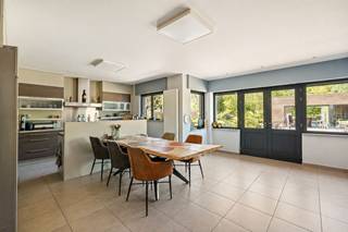 Deze hedendaagse woning is zeer ruim gebouwd in 2007 en is voorzien van een multifunctioneel bijgebouw van 75m² wat veel mogelijkheden biedt voor een zelfstandig ondernemer of hobbyist. Deze eigendom bestaat uit keuken, wasplaats, woonkamer, 6 slaapkamers, bureauruimte, 2 badkamers, volledige onderkeldering die omgevormd kan worden tot mancave, hobbyruimte, bureau etc., bijgebouw met extra badkamer, carport en tuin met vijver.<br /><br />Gelijkvloers:<br />De woning is te betreden via de ruime inkomhal die toegang geeft tot de leefgedeeltes. Deze zijn opgedeeld in een gezellige zithoek met speksteenkachel en een moderne leefkeuken met kwalitatieve toestellen van Siemens en Miele (microgolf, stoomoven, grillplaat, keramisch vuur, grote koelkast, vaatwasmachine en dubbele lavabo). Overigens bevinden er zich hier 2 ruimtes die gebruikt kunnen worden volgens de noden van de koper (bureau, speelkamer, hobbykamer, etc).<br />Op de gelijkvloerse verdieping is er eveneens een wasplaats voorzien die geïnstalleerd is met extra inloopdouche en lavabomeubel. Alsook een achterinkom met apart toilet en bergruimte.<br /><br />Eerste verdieping: <br />De moderne trap brengt ons tot de eerste verdieping die voorzien is van een ruime nachthal. Op deze hal geven 4 volwaardige slaapkamers uit, alsook een zeer ruime badkamer met dubbele lavabo, ligbad, inloopdouche en toilet.<br /><br />Tweede verdieping:<br />Via een vaste trap betreedt u de tweede verdieping. Hier bevinden er zich eveneens 2 extra slaapkamers met een overloop die volledig is afgewerkt met ingemaakte kasten.<br /><br />Tuin:<br />De royale tuin is aangelegd en volledig omheind. Op het perceel is een zeer praktisch bijgebouw voorzien van 75m². Deze is ingedeeld in een mutifunctionele ruimte, badkamer met douche, lavabo en toilet en is eveneens volledig onderkelderd. De ruimte kan verwarmd worden mbv een pelletkachel. De kelder wordt momenteel gebruikt als regenwaterput. Dit bijgebouw is uitgebreid met een hoge carport. Voorts is het perceel aangelegd met een fraaie vijver die mogelijk tot zwembad kan omgevormd worden.<br /><br />Bijzonderheden:<br />- Multifunctioneel bijgebouw van 75m² met onderkeldering (momenteel regenput van 150.000l)<br />- Energiezuinige woning (EPC A) met aanwezigheid 36 zonnepanelen (deels met groenestroomcertificaten)<br />- Conforme elektriciteit<br />- 6 slaapkamers + 2 bureau's/7e en 8e slaapkamer<br />- Volledige onderkeldering die afgewerkt kan worden tot mancave, hobbyruimte, bureau etc. met zowel toegang via de woning als de tuin