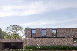 Deze stijlvolle, moderne villa uit 2018 is gelegen op een uitzonderlijk breed perceel van maar liefst 5.016 m² en biedt een unieke combinatie van hedendaags wooncomfort, privacy en een groene, landelijke omgeving. De tijdloze architectuur, gekenmerkt door grote raampartijen, zorgt voor een overvloed aan natuurlijk licht en creëert een harmonieuze verbinding tussen binnen en buiten.<br /><br />Het royale perceel vormt een absolute meerwaarde voor wie houdt van ruimte en natuur. Dankzij de omvang en de rustige ligging biedt het tal van mogelijkheden voor dierenliefhebbers en paardenliefhebbers, met voldoende plaats om dieren aan huis te houden of het terrein naar eigen wens in te richten.<br /><br />Ook voor wie wonen en werken wil combineren, is deze woning bijzonder geschikt. Er zijn twee afzonderlijke ruimtes voorzien die perfect kunnen dienen als praktijk, bureau of kantoor aan huis.<br /><br />De leefruimte werd ontworpen met oog voor openheid, licht en wooncomfort. De volledig uitgeruste keuken is voorzien van hoogwaardige Gaggenau-toestellen en een Quooker-kraan. Vanuit de keuken en de aangrenzende leefruimte geniet u van een prachtig, weids uitzicht over de zuidoost georiënteerde tuin en de achterliggende natuur, waardoor elk seizoen optimaal beleefd kan worden.<br /><br />Aansluitend aan de keuken bevindt zich een ruime berging die eveneens rechtstreeks bereikbaar is via de carport. Daarnaast beschikt de woning over talrijke maatkasten, een tweede grote berging en een aparte wasruimte met douche, waardoor functionaliteit en opbergruimte ruimschoots aanwezig zijn.<br /><br />Het wooncomfort wordt verder versterkt door een uitgebreid domoticasysteem, camerabewaking, een alarmsysteem en een geïntegreerde muziekinstallatie die doorheen de volledige woning voor extra gebruiksgemak en sfeer zorgen.<br /><br />De villa telt vijf volwaardige slaapkamers en twee stijlvolle badkamers. De master bedroom beschikt over een ensuite badkamer en een ruime dressing, met een rustgevend uitzicht op het omliggende groen.<br /><br />Ook op technisch vlak voldoet deze woning aan de hoogste verwachtingen. Dankzij het gunstige energielabel A en de conforme elektrische installatie is deze villa volledig klaar voor de toekomst.<br /><br />Deze uitzonderlijke eigendom biedt een zeldzame combinatie van moderne architectuur, hoogwaardig wooncomfort, een prachtig natuurzicht en een royaal perceel met tal van mogelijkheden voor gezinnen, zelfstandigen én dieren- of paardenliefhebbers.