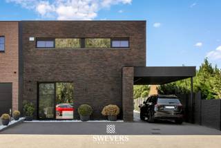 Voor meer info en foto’s, surf naar www.swevers.be – In het hart van Heusden-Zolder vinden we deze instapklare en luxueus afgewerkte halfopen woning uit 2021. Met 226 m² bewoonbare oppervlakte biedt deze gezinswoning vier ruime slaapkamers, een royale leefruimte én een multifunctionele veranda die momenteel dienstdoet als kinderdagverblijf – perfect voor wie wonen en werken wil combineren. De open leefruimte van 50 m² sluit naadloos aan op de moderne keuken van 17 m², compleet met aansluitende berging. Een extra slaapkamer op het gelijkvloers is ideaal als kantoor of praktijkruimte. De ruime veranda achteraan is lichtrijk en biedt tal van mogelijkheden voor professionele of privédoeleinden. Boven zijn er vier slaapkamers, waaronder een master van 22,5 m². De andere kamers zijn tussen 10 en 13 m² groot. De badkamer is volledig uitgerust met moderne voorzieningen. Hoewel de woning geen kelder of zolder heeft, zorgt de slimme indeling voor voldoende opbergruimte. Op het perceel van 5a 66ca geniet je van een zuidoostelijk georiënteerde tuin met zon vanaf de ochtend. Extra troeven zijn airco, alarmsysteem met camera’s, videofoon en zonnepanelen. Dankzij de centrale ligging zijn scholen, winkels, openbaar vervoer en snelwegen snel bereikbaar. Voor meer informatie, bel 011 255 155. Bron bewoonbare oppervlakte: EPC – verslag.