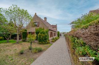 Een royale villa met karakter, privacy en tal van mogelijkheden, gelegen in een rustige residentiële omgeving van Oostduinkerke.<br /><br />Deze vrijstaande woning uit 1987 staat op een uitzonderlijk ruim perceel van 1.165 m² en beschikt over circa 319 m² bewoonbare oppervlakte. Met vier slaapkamers, een dubbele inpandige garage, een veranda, bureau, atelier en verschillende bergruimtes biedt de woning een bijzonder ruim en veelzijdig woonvolume.<br /><br />Bij binnenkomst leidt de inkomhal naar de verschillende leefruimtes. De royale woon- en eetkamer vormt het hart van de woning en sluit aan op de keuken en veranda. Dankzij de verschillende oriëntaties geniet de villa van een aangename natuurlijke lichtinval.<br /><br />Het gelijkvloers omvat daarnaast een bureau, atelier, stookruimte, toilet en een ruime dubbele garage. Ideaal voor wie thuis werkt, een hobbyruimte wenst of nood heeft aan extra bergruimte.<br /><br />Op de verdieping bevinden zich vier slaapkamers, een badkamer, dressing en een nachthal. Daarnaast is er een zolder van circa 40 m², momenteel ingericht als bergruimte.<br /><br />De woning wordt omringd door een ruime tuin en beschikt over een lange oprit, meerdere tuinhuizen en bijgebouwen. Er is dan ook voldoende plaats voor meerdere wagens en tal van buitenactiviteiten.<br /><br />De villa ligt in een aangename woonomgeving, op korte afstand van winkels, horeca, scholen, sport- en recreatiefaciliteiten, natuurgebieden en het strand.<br /><br />De woning verkeert momenteel in een op te frissen staat, waardoor u de verschillende ruimtes en afwerking naar eigen smaak kunt moderniseren.<br /><br />De villa beschikt over centrale verwarming op aardgas, een houtkachel en een regenwaterput van meer dan 10.000 liter. EPC-label C – 260 kWh/m²/jaar.<br /><br />
