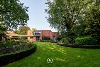 This unique architect's villa was built in 1976 and designed by architect Jan Vangheluwe. The total area of the plot is about 6000 m² with a living area of no less than 1057 m². The villa is characterised by rounded volumes and a beautiful green garden.<br /><br />Upon entering the villa, we enter a large entrance hall with guest toilet and cloakroom. <br />Central to the house is the kitchen, with storage room and cold room, which enjoys a beautiful view over the garden. Adjacent is the dining area with living room that opens onto the terrace. <br />Furthermore, there are three spacious children's bedrooms with study, a spacious bathroom, a guest bedroom with its own bathroom, a spacious master bedroom with dressing room and ensuite bathroom and a very practical laundry room.<br />The first floor includes a space that can be transformed into a hobby room or extra bedroom.<br />Finally, there is a huge multipurpose room of no less than 200 m² that can serve as office space, meeting room, reception room... <br /><br />Additional assets <br />- Double garage <br />- Spacious cellar <br />- Possibility of practising a liberal profession <br />- Plenty of parking space on the plot