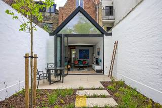 Een schilderachtige locatie in het beschermde stadsgezicht van Dijver, Arentshuis, Gruuthuse en Onze-Lieve-Vrouwkerk. De straat Groeninge vinden we reeds in 1200 terug in de annalen. Het is een gekasseide straat met kronkelend patroon, in het hart van de ‘Gouden Driehoek, weg van alle drukte. De totaalrenovatie van de trapgevelwoning die we hier uitzonderlijk te koop kunnen aanbieden heeft lange tijd geduurd. Het resultaat - een ontwerp van het gekende Brugse architectenbureau Dugardyn – mag dan ook  ‘a piece or art’ genoemd worden, volledig in de lijn van het Brusk museumproject met feeëriek park dat in het verlengde van de woning wordt gerealiseerd. Een absolute topaanbieding dus. Bij de verbouwing van werd het pand volledig gestript en heropgebouwd met behoud van een aantal originele elementen/balken/roosteringen en een nieuwe uitbouw op het gelijkvloers met een opvallend zinken dak in bootvorm. Het pand heeft overal massieve parketvloeren, gezandstraalde trap en geniet van mooie plafondhoogtes met balken en een prima lichtinval. Gelijkvloers : inkom met wanden/deur in staal/glas, toilet met lavabo, trap, volledig ingerichte keuken aan de straatkant met oa inductiekookplaat met Borasysteem, frigo/diepvries, warme luchtoven, vaatwas Bosch, veel en handige kasten, diepe living met grote glaspartij achteraan (vouwramen die volledig open kunnen gezet worden zodat binnen- en buitengebeuren naadloos in elkaar overlopen, driehoekig vast raam bovenaan), schouw met gashaard (afstandsbediening), deur staal/glas naar berging/wijnkelder, terras en hard-landscaping tuin met gekaleide muren en verlichting, externe stroom- en watervoorziening. Tussenverdiep tussen 0 en 1 : kleine overloop met enkele ingemaakte kastjes. 1<sup>ste</sup> Verdieping : overloop, toilet met lavabo, berging/technische ruimte met oa cv condensketel gas, omvormer zonnepanelen, aansluiting voor wasmachine en droogkast, masterbedroom aan de tuinkant, badkamer aan de straatkant met diepe inloopdouche (marmer), breed lavabomeubel met 2 opstaande lavabo’s, spiegel met led-verlichting. 2<sup>de</sup> Verdieping : overloop, toilet met lavabo, 2 mooie slaapkamers (knap dakgebinte gedeeltelijk zichtbaar). CV gas. Enkele weetjes/eye)catchers : de uitbouw heeft een zelden gezien dak in de vorm van een bootromp met zinken buitenkant, isolatie en energie-efficiëntie volgens hoge normen, inclusief 6 zonnepanelen, quasi overal nieuwe ramen met driedubbele beglazing, nieuw dak, verbeterde isolatie, overal laagspanningsverlichting, akoestische isolatie van de tussenmuren, veiligheidstrapverlichting, overal bijpassende verlichtingsarmaturen, alarm- en verwarmingscontrolesystemen via internet. Niet gelegen in overstromingsgevoelig gebied. G-score: A, P-score: A