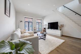 Rustig wonen in het hart van Turnhout, met alle voorzieningen op wandelafstand? Dit lichtrijke en instapklare eigendom vormt een unieke combinatie tussen een bel-etage en een duplexappartement. De royale woonoppervlakte (163m2), de verschillende niveaus en de vele praktische ruimtes zorgen voor bijzonder veel mogelijkheden en een uiterst aangenaam woongevoel.

Het appartement werd grondig gerenoveerd. In 2018 werden onder meer de keuken, de badkamer en het afzonderlijke toilet volledig vernieuwd. De condenserende gasketel dateert van 2017 en in 2019 werd een lucht-luchtwarmtepomp met verwarmings- en aircofunctie geplaatst. Het geheel werd zorgvuldig onderhouden en is werkelijk instapklaar.

Op de eerste verdieping bevindt zich de ruime en lichtrijke leefruimte met grote raampartijen en een stijlvolle parketvloer. De living biedt alle ruimte voor een volwaardige zit- en eethoek en sluit mooi aan op de open, volledig ingerichte keuken. Deze beschikt over veel kastruimte, een royaal werkblad en een praktische inrichting.

De ruime slaapkamer is eveneens afgewerkt met parket en beschikt over een prachtige dressing en rechtstreekse toegang tot het terras. De handige mezzanine biedt bijkomende mogelijkheden als logeerplek, leeshoek of extra bergruimte.

De tijdloze badkamer is ingericht met een dubbele wastafel, een ligbad en een afzonderlijke douche. Daarnaast is er een apart toilet met eigen wastafel.

Via de trap vanuit de woonkamer bereikt u de tweede verdieping, waar zich een royale polyvalente kamer bevindt (extra slaapkamer, bureau, of hobbyruimte).

Op het gelijkvloers beschikt het eigendom over een garage met automatische poort (verplicht samen met het appartement te worden aangekocht).

Daarnaast is er een uitzonderlijk ruim en polyvalent magazijn met een hoge industriële toegangspoort. Deze ruimte is ideaal voor opslag van materiaal/voertuigen of uitgebreid hobbygebruik en vormt een bijzonder zeldzame meerwaarde op deze centrale locatie.

Verder beschikt het appartement over zonnepanelen, een condenserende gasketel en een lucht-luchtwarmtepomp, wat leidt tot een gunstige EPC B-score.

Een uniek eigendom voor wie centraal en stijlvol wil wonen, met het comfort en de beleving van een woning, gecombineerd met de praktische voordelen van een duplexappartement.

Vraagprijs appartement: € 275.000
Garage met automatische poort, verplicht bij aan te kopen: € 30.000
Ruim magazijn met industriële poort: € 55.000