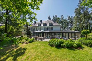 <p><strong>Deze uitzonderlijke villa is gelegen op een perceel van ca. 4.950 m² langs de Antwerpsesteenweg in Vosselaar en combineert aanzienlijke volumes met een doordachte indeling. De royale inkomhal biedt toegang tot de leefruimtes, bestaande uit een eet- en zithoek, een afzonderlijke tv-kamer en een bureauruimte. Centraal bevindt zich de vernieuwde keuken met Gaggenau-toestellen, uitgevend op het overdekte binnenzwembad, een lichtrijke leefruimte met tuincontact en een wellnessgedeelte met sauna. Verder beschikt de woning over een inpandig duplex appartement met eigen ingang, een totaal van acht slaapkamers en zes badkamers. </strong><br /><br /><strong><span>Indeling</span><br /></strong>Via de imposante entreehal betreedt u de woning. Aan de linkerzijde bevindt zich een eerste leefruimte die is ingericht met eet- en zitgelegenheid. Aansluitend volgt een afzonderlijke tv-kamer, met daarnaast een bijkomende ruimte die zich leent tot gebruik als bureau of werkkamer.</p>
<p>Het hart van de villa is de keuken, welke zich centraal in de villa bevindt. De keuken werd enkele jaren geleden vernieuwd en is uitgerust met kwalitatieve Gaggenau-toestellen. De keuken kijkt uit op het overdekte binnenzwembad en op een aangrenzende, lichtrijke ruimte met glazen dak, ingericht als eet/leefruimte en in direct contact met de tuin. De keuken alsook de ruimte met binnenzwembad verlenen toegang tot de kelderverdieping. Deze heeft een gedeeltelijke barfunctie en een wellnessfunctie, compleet met sauna en douches.</p>
<p>Verder op het gelijkvloers bevinden zich een vestiaire, een gastentoilet en een wasplaats. Vanuit de wasplaats is er toegang tot de ruime garage, voorzien van meerdere poorten aan voor- en achterzijde.<br /><br /><strong><span>Verdieping</span></strong><br />Op de eerste verdieping, dewelke we bereiken via de royale wenteltrap, bevinden zich drie slaapkamers, elk met bijhorende badkamer. De mastersuite, met royale afmetingen, is uitgerust met twee dressings. De tweede verdieping omvat nog twee bijkomende slaapkamers, een speelkamer, een extra badkamer en zolderruimte.<br /><br /><strong><span>Appartement</span></strong><br />In het pand is tevens een volwaardig inpandig appartement ondergebracht, opgevat als duplex en geschikt voor conciërge of inwonende ondersteuning. Dit appartement beschikt over een leefruimte, keuken, 2 badkamers en 3 slaapkamers, en functioneert autonoom binnen het geheel met eigen ingang.</p>
<p>De villa beschikt in totaal over 8 slaapkamers en 6 badkamers, en biedt een bewoonbare oppervlakte van ca. 1.436 m² (inclusief appartement). Het geheel wordt omgeven door een ruim, groen perceel dat privacy en rust waarborgt, met behoud van een vlotte bereikbaarheid.</p>
<p>Een eigendom met aanzienlijke volumes en diverse gebruiksmogelijkheden, geschikt voor wie ruimte, comfort en een zekere autonomie binnen het wonen weet te waarderen. Verder biedt de woning nog de mogelijkheid voor andere invullingen, zoals bv. B&B, kleinschalig restaurant, kantoor (bv. private banking) of een andere, rustige, zelfstandige activiteit.<br /><br /><span><strong>Bijzonderheden:</strong></span><br />- Riant perceel van ca. 4950m<span>²</span><br />- Totaliteit van 8 slaapkamers en 6 badkamers<br />- Indoor zwembad met welness<br />- Royale ruimtes met doordachte indeling<br />- Gunstige ligging nabij invalswegen en vlotte bereikbaarheid naar zowel Nederland als Antwerpen.</p>