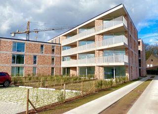 De assistentiewoning krijgt in Villa Moeie een geheel nieuwe dimensie. Grote glaspartijen vloeien moeiteloos over in een strak gebouw. Ruime, overdekte terrassen maken het mogelijk om optimaal van het buitenleven te genieten. Dit gevoel wordt versterkt door de gezamenlijke tuin, waar men onder het tuinpaviljoen kan samenkomen voor een drankje of een babbel. De groene vingers zijn in de nabijgelegen moestuin in hun sas. Sportievelingen vinden zeker hun gading aan de petanquebaan.
Dit nieuwbouwproject omvat 2 gebouwen, het villagebouw en het residentiegebouw. Beiden beschikken over een eigen technische ruimte en fietsenstalling. Hier kunnen ook scootmobiels gestald en opgeladen worden.
In het residentiegebouw op de hoek van de Moeie en de Tieltsesteenweg, worden 27 assistentiewoningen afgewisseld met gemeenschappelijke ruimtes. Hier is onder meer het bureau van de woonassistent gevestigd. Daarnaast is er ook een ontmoetingsruimte met bar en salon, bezoekerstoilet en afvalberging.
Het aparte villagebouw bestaat uit 8 assistentiewoningen, en evenveel private kelders.
De 34 parkeerplaatsen zijn als volgt verdeeld:
- 3 parkeerplaatsen voor zorgverstrekkers en woonassistenten
- 2 (minder)valide bezoekersparkeerplaatsen
- 29 privatieve parkeerplaatsen met gepersonaliseerde beveiligde toegang.
Elke flat heeft een eigen water- en elektriciteitsteller, inbraakwerende voordeur en warmtepomp. Een afzonderlijke inkomhal zorgt voor privacy, de open keuken in de lichtrijke leefruimte maakt het aangenaam om familie en vrienden te ontvangen. De slaapkamers zijn royaal van grootte, zodat een dubbel bed én een kast er makkelijk passen. In de badkamer zijn discreet hulpmiddelen aangebracht, zoals een zitje in de douche en een handgreep naast het toilet.
Het gehele park is rolstoeltoegankelijk. Doorheen het appartement kan de bewoner een alarm activeren, of de zorgassistent bereiken voor meer hulp. Kortom, sfeer, comfort en hulp waren nog nooit zo toegankelijk!
Wenst u meer info over dit unieke project?
Bel dan Nic van Unicum voor een verhelderend gesprek op 09 336 16 15.