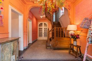 <p><strong>Op een centrale locatie in het hart van Kasterlee bevindt zich dit uitzonderlijk karaktervol eigendom, momenteel gekend als Boudoir D’or. Dit stijlvolle burgerhuis combineert een authentieke uitstraling met tal van mogelijkheden voor wonen, werken en ondernemen. De statige voorgevel met markante erker geeft het eigendom een sterke visibiliteit en unieke uitstraling in het straatbeeld. Binnenin zorgen bewaarde karakterelementen, zoals parketvloeren, glas-in-loodramen, hoge plafonds, rozetten en moulures, voor een warme sfeer. Dankzij de indeling en centrale ligging leent dit eigendom zich uitstekend voor diverse invullingen: handelspand met woonst, kantoorruimte, praktijkruimte, showroom, vrij beroep of een stijlvolle combinatie van wonen en werken. De authentieke architectuur geeft elke professionele activiteit extra uitstraling. Bovendien geniet het eigendom van een uitstekende bereikbaarheid, met voorzieningen in de directe omgeving en parkeermogelijkheden op eigen terrein, achteraan bereikbaar via de Markt. Dit vormt een belangrijke troef voor bewoners, klanten en bezoekers.<br /><br /></strong><span>Gelijkvloerse verdieping</span>: Op de gelijkvloerse verdieping wordt men verwelkomd in een stijlvolle inkomhal met prachtige authentieke trap. Het voorste gedeelte is momenteel ingericht als kledingszaak en geniet, dankzij de centrale ligging en zichtbaarheid in het straatbeeld, van een sterke commerciële uitstraling.<br /><br />Achterliggend bevindt zich het private woongedeelte met gezellige woonkamer en aansluitende keuken. De indeling laat toe om wonen en werken comfortabel te combineren. Vanuit dit achterste gedeelte is er via een vaste trap toegang tot de bovenverdieping, zonder door de kledingszaak te moeten gaan. Zo ontstaat een duidelijke scheiding tussen het professionele gedeelte vooraan en het private gedeelte achteraan.<br /><br />De woonkamer beschikt over een open haard op gas. De keuken is uitgerust met een Godin kookvuur op gas, extra oven, koelkast en diepvries. Langs de achterzijde is er toegang tot de tuin. Verder biedt deze verdieping toegang tot de kelder.<br /><br /><span>Eerste verdieping</span>: Op de eerste verdieping bevinden zich twee ruime slaapkamers. De masterbedroom beschikt over airco, dressing en ensuite badkamer. Daarnaast zijn er momenteel een woonkamer en eetkamer ingericht, die ook perfect kunnen dienen als bijkomende slaapkamer, hobbykamer, bureau, wachtruimte, praktijkruimte of polyvalente ruimte. Tot slot is er nog een extra kamer met toilet en wastafel. Dankzij de ruimte kan hier indien gewenst ook een douche worden geplaatst, waardoor een bijkomende badkamer mogelijk is. Via een vaste trap is er toegang tot een ruime zolderkamer met tal van mogelijkheden.<br /><br /><span>Buitengebeuren:</span> Achteraan beschikt het eigendom over een gezellige tuin met aangenaam terras. De tuin is zowel langs de zijkant toegankelijk, praktisch voor fietsen en/of containers, als via de achterzijde dankzij een servitude via de Markt, die bij de woning hoort. Hierdoor kan men ook met de wagen tot op het perceel rijden. Momenteel zijn er achteraan twee private autostaanplaatsen voorzien, een belangrijke troef voor bewoners, klanten en bezoekers. <br /><br />Verder bevindt zich achteraan een ruim bijgebouw/magazijn, ideaal als extra opslagruimte voor de huidige kledingszaak, stockageruimte, werkplaats, hobbyruimte of ondersteunende ruimte voor een zelfstandige activiteit aan huis. Aansluitend is er bovendien nog een overdekt terras aanwezig.<br /><br /><span>Bijzonderheden:</span> <br />- Volledig onderkelderd <br />- Verwarming op mazout d.m.v. radiatoren <br />- Ruim magazijn <br />- EPC: 575 Kwh/m²/j <br /><br />Bekijk dit eigendom via onze virtual tour: https://tour.giraffe360.com/9382448a8b8d45bc8def99252a3bdcf5</p>