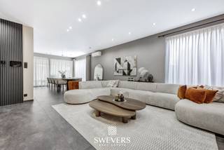 Voor meer info en foto’s, surf naar www.swevers.be – In het hart van Heusden-Zolder vinden we deze instapklare en luxueus afgewerkte halfopen woning uit 2021. Met 226 m² bewoonbare oppervlakte biedt deze gezinswoning vier ruime slaapkamers, een royale leefruimte én een multifunctionele veranda die momenteel dienstdoet als kinderdagverblijf – perfect voor wie wonen en werken wil combineren. De open leefruimte van 50 m² sluit naadloos aan op de moderne keuken van 17 m², compleet met aansluitende berging. Een extra slaapkamer op het gelijkvloers is ideaal als kantoor of praktijkruimte. De ruime veranda achteraan is lichtrijk en biedt tal van mogelijkheden voor professionele of privédoeleinden. Boven zijn er vier slaapkamers, waaronder een master van 22,5 m². De andere kamers zijn tussen 10 en 13 m² groot. De badkamer is volledig uitgerust met moderne voorzieningen. Hoewel de woning geen kelder of zolder heeft, zorgt de slimme indeling voor voldoende opbergruimte. Op het perceel van 5a 66ca geniet je van een zuidoostelijk georiënteerde tuin met zon vanaf de ochtend. Extra troeven zijn airco, alarmsysteem met camera’s, videofoon en zonnepanelen. Dankzij de centrale ligging zijn scholen, winkels, openbaar vervoer en snelwegen snel bereikbaar. Voor meer informatie, bel 011 255 155. Bron bewoonbare oppervlakte: EPC – verslag.