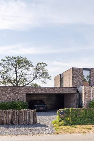 Deze stijlvolle, moderne villa uit 2018 is gelegen op een uitzonderlijk breed perceel van maar liefst 5.016 m² en biedt een unieke combinatie van hedendaags wooncomfort, privacy en een groene, landelijke omgeving. De tijdloze architectuur, gekenmerkt door grote raampartijen, zorgt voor een overvloed aan natuurlijk licht en creëert een harmonieuze verbinding tussen binnen en buiten.<br /><br />Het royale perceel vormt een absolute meerwaarde voor wie houdt van ruimte en natuur. Dankzij de omvang en de rustige ligging biedt het tal van mogelijkheden voor dierenliefhebbers en paardenliefhebbers, met voldoende plaats om dieren aan huis te houden of het terrein naar eigen wens in te richten.<br /><br />Ook voor wie wonen en werken wil combineren, is deze woning bijzonder geschikt. Er zijn twee afzonderlijke ruimtes voorzien die perfect kunnen dienen als praktijk, bureau of kantoor aan huis.<br /><br />De leefruimte werd ontworpen met oog voor openheid, licht en wooncomfort. De volledig uitgeruste keuken is voorzien van hoogwaardige Gaggenau-toestellen en een Quooker-kraan. Vanuit de keuken en de aangrenzende leefruimte geniet u van een prachtig, weids uitzicht over de zuidoost georiënteerde tuin en de achterliggende natuur, waardoor elk seizoen optimaal beleefd kan worden.<br /><br />Aansluitend aan de keuken bevindt zich een ruime berging die eveneens rechtstreeks bereikbaar is via de carport. Daarnaast beschikt de woning over talrijke maatkasten, een tweede grote berging en een aparte wasruimte met douche, waardoor functionaliteit en opbergruimte ruimschoots aanwezig zijn.<br /><br />Het wooncomfort wordt verder versterkt door een uitgebreid domoticasysteem, camerabewaking, een alarmsysteem en een geïntegreerde muziekinstallatie die doorheen de volledige woning voor extra gebruiksgemak en sfeer zorgen.<br /><br />De villa telt vijf volwaardige slaapkamers en twee stijlvolle badkamers. De master bedroom beschikt over een ensuite badkamer en een ruime dressing, met een rustgevend uitzicht op het omliggende groen.<br /><br />Ook op technisch vlak voldoet deze woning aan de hoogste verwachtingen. Dankzij het gunstige energielabel A en de conforme elektrische installatie is deze villa volledig klaar voor de toekomst.<br /><br />Deze uitzonderlijke eigendom biedt een zeldzame combinatie van moderne architectuur, hoogwaardig wooncomfort, een prachtig natuurzicht en een royaal perceel met tal van mogelijkheden voor gezinnen, zelfstandigen én dieren- of paardenliefhebbers.
