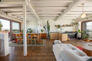 <strong>Algemeen</strong><br />Op de zesde en zevende verdieping, helemaal bovenaan het gebouw, ligt dit duplex-penthouse van ca. 211 m². Het voelt eerder als een huis in de lucht dan als een appartement. Beneden is het rustig, met drie slaapkamers, een aparte dressing, een badkamer en veel ingemaakte kasten. Boven ligt één grote, lichte leefruimte met witgeschilderde balken, een industriële keuken, een vierde slaapkamer, een tweede badkamer en twee terrassen van samen zo’n 70 m². Een smeedijzeren wenteltrap verbindt de twee verdiepingen. Ook technisch zit het goed: het dak van het gebouw werd gerenoveerd, de verwarmingsketel is pas vernieuwd en het appartement heeft een EPC-label C. Er is een lift, en bij het appartement horen twee kelders.<br /><strong>Ligging</strong><br />Het penthouse ligt aan het begin van de Turnhoutsebaan, op het kruispunt met de Carnotstraat en de Kerkstraat. Het Centraal Station, het Astridplein en de Zoo liggen op een paar minuten wandelen. Winkels, bakkers, koffiebars en restaurants vind je in alle richtingen, en tram en bus stoppen vlakbij. Je woont hier in het hart van de stad, maar vanaf de bovenste verdieping hoor je de drukte nauwelijks en zie je vooral daken, kerktorens en veel lucht.<br /><strong>Indeling</strong><br />Zesde verdieping: de nachtverdieping<br />Je komt binnen in een ruime inkomhal met een marmeren vloer en een hele wand ingemaakte kasten, zodat jassen, schoenen en tassen meteen uit het zicht zijn. Vanuit de hal bereik je alle ruimtes op deze verdieping.<br />Op deze verdieping liggen drie slaapkamers. De grootste is een echt ruime kamer met een groot raam en een deur naar het balkon, vanwaar je over de daken en het groen van de buurt kijkt. De tweede slaapkamer is nu ingericht als bureau. Een groot raam zorgt voor veel daglicht en de witgeschilderde bakstenen muur geeft de kamer karakter. De derde slaapkamer is even rustig en ruim, en elke kamer heeft eigen kastruimte. Daarnaast is er een aparte dressing met een eigen raam, dat uitkijkt op de kerktoren. Zo heb je kleding en schoenen netjes uit de slaapkamers. Op de hele verdieping, behalve in de inkomhal, ligt eiken mozaïekparket. De korte stroken liggen per vier in vierkantjes, telkens een kwartslag gedraaid zoals een dambord. Het is een klassieker die mooi verweerd is en de kamers meteen warmte geeft.<br />De badkamer op deze verdieping is sober en strak. De douche heeft grote antracietkleurige tegels, een regendouche met handdouche en een glazen schuifdeur. Het aparte toilet ligt ernaast.<br />De wenteltrap<br />Vanuit de inkomhal loop je via een smeedijzeren wenteltrap naar boven. Wie omhoog kijkt, ziet een ronde trapopening met een sierlijke balustrade vol krullen en daarboven de witte balken van de leefruimte. Het is een van die details die je nergens anders tegenkomt.<br />Zevende verdieping: de leefverdieping<br />Boven kom je uit in het hart van de woning: één grote leefruimte van meer dan twaalf meter lang. Het plafond heeft witgeschilderde houten balken en aan meerdere kanten zijn er ramen, waardoor er van ‘s ochtends tot ‘s avonds licht binnenvalt. De ronde trapopening staat midden in de ruimte en verdeelt ze vanzelf in zones zonder dat er muren nodig zijn. Aan de ene kant is er plaats voor een grote zithoek, met een witte nis in de muur en een stuk witgeschilderde baksteen die er een gezellige hoek van maken. Aan de andere kant staat de eettafel voor een groot raam met houten schuiframen, die rechtstreeks uitkomen op het terras.<br />De keuken is industrieel ingericht: witte metrotegels tot aan het plafond, een stoer professioneel fornuis met grote oven, een roestvrijstalen dampkap met zichtbare afvoerbuis, open rekken in staal en hout en een magneetstrip voor de messen. De dubbele spoelbak staat onder een breed raam, zodat je bij de afwas over de stad kijkt. Het is een keuken voor mensen die graag en veel koken.<br />Dan de terrassen. Het zuidwestterras van ca. 40 m² krijgt de zon in de namiddag en ‘s avonds. Het noordoostterras van ca. 30 m² is ideaal voor een ontbijt in de ochtendzon of als koele plek op warme zomerdagen. Op het terras liggen terrazzotegels en rondom staat een witgeschilderde bakstenen borstwering. Het uitzicht reikt over de daken tot aan de skyline van Antwerpen.<br />Op deze verdieping ligt ook de vierde slaapkamer, een rustige kamer met sierlijsten aan het plafond. De tweede badkamer is een echte eyecatcher. De wanden zijn bekleed met handgemaakte, glanzende tegeltjes in zachte grijsblauwe tinten, en er is een ligbad, een inloopdouche met regendouche, een lange brede wastafel met een grote spiegelkast en een handdoekradiator. Door het raam valt daglicht binnen. Verder is er een apart toilet en een berging die als wasplaats is ingericht.<br />De hele bovenverdieping heeft een bamboevloer met de typische knopen in het hout, die een ander karakter heeft dan het parket beneden. In de leefruimte zijn de vloerconvectoren weggewerkt onder houten lattenroosters, zodat er geen radiatoren tegen de muren staan.<br /><strong>Troeven</strong>
<ul>
<li>Duplex-penthouse van ca. 211 m² op de 6e en 7e verdieping</li>
<li>Twee terrassen: zuidwest (ca. 40 m²) en noordoost (ca. 30 m²), met weids zicht over Antwerpen</li>
<li>Leefruimte van ruim 2 m1 met witgeschilderde balken en veel lichtinval</li>
<li>Industriële keuken met professioneel fornuis</li>
<li>4 ruime slaapkamers (3 op de 6e, 1 op de 7e), een dressing en veel ingemaakte kasten</li>
<li>2 volwaardige badkamers (één per verdieping) en 2 aparte toiletten</li>
<li>Smeedijzeren wenteltrap als blikvanger</li>
<li>Eiken mozaïekparket op de 6e verdieping, bamboe op de 7e, marmer in de inkomhal</li>
<li>Vloerconvectoren in de leefruimte</li>
<li>Gerenoveerd dak, nieuwe verwarmingsketel, EPC C</li>
<li>Lift en 2 kelders</li>
<li>Op wandelafstand van het Centraal Station</li>
</ul>
De grondplannen, het EPC en de asbestinventaris vind je onder “Documenten” op onze website. Kom het uitzicht zelf bekijken en maak een afspraak via info@wellimmo.net of op 03 225 00 68.