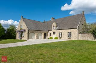 Ruime villa op ca. 4.500m² bestaande uit inkomhal, ruime living met open haard, bibliotheek en eetplaats, ruime ingerichte keuken, wasplaats, berging, 6 slaapkamers en badkamer. Dubbele garage met hobbykamer (mancave) boven deze garage, volledig onderkelderd, zolder, terrassen en zeer mooie tuin. Mogelijkheid +/- 5.500m² aangelegde tuin met grote tuinberging bij te kopen (woonuitbreidingsgebied).