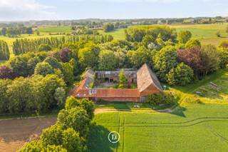 Te midden van een prachtig groen domein van ca. 3 hectare, bereikbaar via een lange private dreef, bevindt zich deze authentieke rustieke vierkantshoeve met uitzonderlijk veel charme en potentieel. De eigendom geniet van volledige rust en privacy, omringd door groene vergezichten, een eigen bos en een idyllische vijver die samen zorgen voor een uniek en sfeervol kader.<br /><br />Deze karaktervolle hoeve vormt de ideale plek voor wie op zoek is naar landelijk wonen met ruimte, authenticiteit en tal van mogelijkheden. Dankzij de combinatie van wooncomfort, royale bijgebouwen en het uitgestrekte perceel leent het geheel zich perfect voor paardenliefhebbers of een combinatie wonen-werken.<br /><br />Het woonhuis is functioneel ingedeeld en beschikt op het gelijkvloers over een inkomhal, gastentoilet, technische ruimte, keuken met eetplaats en een gezellige leefruimte met zicht op het omliggende groen. Op de eerste verdieping bevinden zich vier volwaardige slaapkamers en twee badkamers. De tweede verdieping biedt bijkomende mogelijkheden dankzij de ruime zolderverdieping.<br /><br />Verder beschikt het domein over een imposante schuur met authentieke eiken balkenstructuur, diverse opslagruimtes en paardenstallen. De charmante binnenkoer vormt het hart van de hoeve en versterkt het unieke karakter van deze eigendom.<br /><br />Een uitzonderlijke opportuniteit voor wie droomt van een karaktervolle hoeve op een absolute toplocatie in alle rust en natuur.
