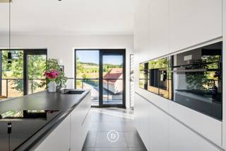 Op een uitzonderlijke locatie aan de voet van de Kanarieberg, met het Muziekbos als indrukwekkend decor, bevindt zich deze recente designvilla uit 2023. De combinatie van hedendaagse architectuur, hoogwaardige afwerking en een panoramisch uitzicht over het omliggende landschap maakt van deze eigendom een bijzonder geheel.<br /><br />De woning werd ontworpen rond licht en openheid. Grote raampartijen brengen het landschap maximaal naar binnen en zorgen voor een voortdurende verbinding met de omgeving. De strakke architectuur wordt daarbij verzacht door een warme en luxueuze interieurafwerking, waardoor een eigentijdse maar aangename woonomgeving ontstaat.<br /><br />Het gelijkvloers is ingericht als private slaap- en werkzone, met drie slaapkamers, een ruime masterbedroom met maatwerkkasten en dressing, een hoogwaardige badkamer en een afzonderlijke bureauruimte. De verdieping vormt het sociale hart van de woning, met een ruime open leefruimte waarin keuken, eetplaats en zithoek harmonieus samenkomen. Vanuit hier geniet men niet alleen van een uitzonderlijke hoeveelheid natuurlijk licht, maar vooral van het continue zicht op het Muziekbos.<br /><br />Het buitenleven sluit hier naadloos op aan. Het ruime terras met luifel en het bijkomende zonneterras bieden verschillende plaatsen om te genieten van de rust en het landschap. De aangelegde tuin, dubbele carport en automatische schuifpoort zorgen voor het nodige comfort en privacy.<br /><br />Ook op energetisch en technisch vlak werd de woning volledig afgestemd op hedendaags wooncomfort, met onder meer een warmtepomp, vloerverwarming, 48 zonnepanelen, een dubbele thuisbatterij, regenwaterrecuperatie, camerabewaking en een laadpaal. Met een EPC-label A combineert de villa haar luxueuze uitstraling met een bijzonder energiezuinig karakter.<br /><br />Een eigendom voor wie hedendaagse architectuur weet te waarderen, maar vooral op zoek is naar een woning met een bijzondere ligging, rust en een uitzicht dat elke dag opnieuw blijft verrassen.
