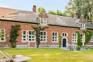Hof ter Saele est situé sur un domaine historique de 52 ares qui faisait autrefois partie des biens féodaux de l’abbaye d’Affligem, avec une histoire de destruction et de reconstruction en 1643. La propriété est accessible par une allée de tilleuls majestueuse, avec un verger attenant d’arbres fruitiers. La maison dégage beaucoup de caractère grâce à des éléments authentiques tels que de hauts plafonds, des sols en pierre naturelle, des structures en poutres de chêne et des cheminées décoratives.<br /><br />La maison offre 488 m² habitables avec de beaux volumes.<br /><br />Au rez-de-chaussée, vous entrez par un hall d’entrée spacieux avec vestiaire et toilette invités. L’aile gauche donne accès à un bureau ou chambre d’amis pouvant servir de chambre supplémentaire, ainsi qu’à une buanderie avec raccordements. L’aile droite s’ouvre sur un séjour chaleureux avec cheminée, relié à la salle à manger et à la cuisine rénovée avec coin petit-déjeuner.<br /><br />À l’étage, un vaste hall de nuit avec placards intégrés et espaces de rangement. Trois chambres, dont une suite parentale avec salle de bain attenante avec baignoire et douche. Les deux autres chambres partagent une salle de bain.<br /><br />La propriété comprend un bâtiment annexe utilisé comme garage avec deux portes d’accès, espace pour deux voitures et rangement. Il dispose aussi d’un grenier pour stockage supplémentaire. Un second petit bâtiment sert de cabane de jardin. La maison est idéalement située sur l’axe Bruxelles–Gand, proche des commerces et écoles. Le jardin orienté plein sud, clôturé et sans vis-à-vis, offre calme et intimité.