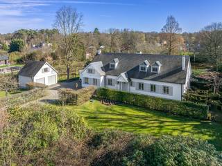 Bij het betreden van de woning komt u in een ruime inkomhal met karaktervolle Bourgondische tegelvloer, die meteen de warme sfeer van de woning zet. Aan de rechterzijde bevindt zich de gezellige leefruimte met authentieke zitput, een ideale plek om in alle comfort te ontspannen.<br /><br />Achteraan de woning bevindt zich een ruime, volledig uitgeruste keuken met Miele-toestellen, die naadloos aansluit op de lichtrijke veranda. Deze veranda is voorzien van airconditioning en biedt een prachtig uitzicht op de fraai aangelegde tuin met vijver, waardoor binnen en buiten harmonieus in elkaar overvloeien.<br /><br />Op het gelijkvloers vindt u verder nog een ruime bureauruimte aan de voorzijde van de woning, perfect geschikt als praktijkruimte of voor wie comfortabel van thuis wil werken. Daarnaast beschikt de woning op dit niveau over een slaapkamer met ensuite badkamer, een praktische wasruimte en een inpandige garage met automatische poort.<br /><br />De verdieping omvat vier slaapkamers. Twee slaapkamers zijn momenteel met elkaar verbonden, maar kunnen eenvoudig opnieuw afzonderlijk gebruikt worden. De derde slaapkamer is bijzonder ruim en de master bedroom beschikt over een eigen badkamer met ligbad en douche, evenals een aparte dressing. De trappenhal is voorzien van ingemaakte kasten, wat zorgt voor een overvloed aan praktische bergruimte.<br /><br />Ook buiten heeft deze eigendom heel wat troeven. De volledig omheinde tuin biedt optimale privacy en is vooraan voorzien van een dubbele garage met daarboven een polyvalente ruimte, die volledig naar eigen wensen kan worden ingericht. De mooi aangelegde vijver en de uitrit achteraan het perceel maken het geheel compleet.<br /><br />Het perceel van 4.974 m² bestaat uit twee bouwgronden, waardoor het achterste gedeelte in de toekomst eventueel kan worden benut voor de bouw van een extra woning. Met een straatbreedte van meer dan 50 meter geniet u bovendien van een uitzonderlijk ruimtelijk gevoel.<br /><br />De woning is uiterst rustig gelegen aan de rand van het Zoerselbos, een ideale omgeving voor wandel- en fietsliefhebbers. Tegelijk bevindt u zich op korte afstand van de op- en afrit van de E34, wat zorgt voor een vlotte bereikbaarheid. Een unieke combinatie van rust, ruimte en bereikbaarheid.