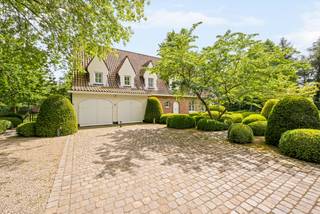 Op een absolute toplocatie in het gegeerde Schilde-Bergen, rustig gelegen nabij St. Ludgardis en omgeven door mature groenaanplantingen, bevindt zich deze perfect onderhouden klassieke villa op een mooi perceel van ca. 2.162 m². De woning biedt royale leefruimtes, 6 slaapkamers, 4 badkamers en een sfeervol bijgebouw achteraan in de tuin. Dankzij de zuidgerichte oriëntatie en de hoogwaardige afwerking is dit een unieke eigendom op één van de meest gegeerde lanen van Schilde.<br /><br />Indeling gelijkvloers:<br />De elegante inkomhal met natuurstenen vloer, vestiaire met gastentoilet en witgelakte trappartij geeft toegang tot de verschillende leefruimtes.<br />De opeenvolging van leefruimtes creëert een heerlijk ruimtelijk gevoel: een zitkamer met openhaard, een aparte eetkamer en een 3e royale leefruimte met grote raampartijen rondom, telkens met zicht op de tuin en directe toegang tot de terrassen.<br /><br />De volledig uitgeruste keuken in tijdloos wit beschikt over een kookeiland, veel kastruimte en kwalitatieve toestellen (o.a. Miele). Aansluitend bevinden zich een praktische voorraadruimte, een ruime wasplaats met ingemaakte kasten, een extra gastentoilet en toegang tot de inpandige dubbele garage.<br /><br />Eerste verdieping:<br />De royale nachthal leidt naar de master suite, bestaande uit een ruime slaapkamer met prachtig tuinzicht over het grote balkon, een volledig ingerichte badkamer met ligbad, inloopdouche, lavabomeubel en toilet, en een uitzonderlijke volledig ingerichte dressing over de volledige lengte.<br /><br />Daarnaast zijn er 3 extra slaapkamers, elk voorzien van ingemaakte kasten, en een bijkomende badkamer met inloopdouche, lavabomeubel en toilet.<br /><br />Tweede verdieping:<br />De tweede verdieping biedt bijkomend woonvolume, met een kleine hal voorzien van linnenkast, 2 ruime slaapkamers waarvan 1 met ingemaakte kasten. Verder is er nog een technische ruimte en een eigen badkamer met inloopdouche, lavabomeubel en toilet.<br /><br />Bijgebouw:<br />Achteraan in de tuin bevindt zich een charmant bijgebouw, volledig opgetrokken in dezelfde klassieke stijl als de woning.<br />Het omvat een inpandige ruimte aan de voorzijde met de installatie voor tuinbesproeiing, een overdekt gedeelte dat geschikt is als zithoekje of voor fietsen, en een achtergedeelte dat gebruikt werd als hondenhok/berging.<br />Via een vaste trap bereikt men de bovengelegen ruimte, ideaal als atelier, speelruimte, kantoor of gastenverblijf.<br /><br />Dit bijgebouw vormt een sterke functionele meerwaarde voor het perceel.<br /><br />Bijzonderheden:<br />- Zuidgerichte, volledig aangelegde en omheinde tuin<br />- Tijdloze architectuur en hoogwaardige afwerking<br />- 6 slaapkamers – 4 badkamers – ruime dressing<br />- Inpandige dubbele garage<br />- Automatische poort<br />- Bijgebouw met diverse gebruiksmogelijkheden