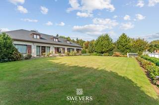 Voor meer info en foto’s, surf naar www.swevers.be – Aan de Helzoldstraat 92 in Houthalen-Helchteren wacht een ruime open bebouwing op een perceel van bijna 40 are. Met een bewoonbare oppervlakte van 412 m² en een kelder van 209 m² is deze woning ideaal voor grote gezinnen, zelfstandigen of wie op zoek is naar extra wooncomfort. De woning werd deels vernieuwd in 2017 (verwarmingsinstallatie, keuken, badkamer, vloeren) en recent in 2024 voorzien van nieuwe ramen en elektrische rolluiken. Op het gelijkvloers tref je een ruime inkomhal, aparte vestiaire, lichtrijke leefruimte van 50 m², een vernieuwde keuken, drie slaapkamers, een badkamer, een apart toilet, een bijkeuken en een bureauruimte. Op de eerste verdieping is een aparte woonunit met leefruimte, keuken, badkamer en grote slaapkamer, perfect voor kangoeroewonen of dubbele bewoning. De kelder met dubbele garage is volledig uitgerust en toegankelijk via 2 sectionale poorten – ideaal als werk- of opslagruimte. Buiten geniet je van een prachtig aangelegde tuin met sproei-installatie, ruime oprit, extra garage en veel privacy. De woning ligt op korte afstand van winkels, scholen, ontspanning en de E314. Voor meer informatie, bel 011 255 155. Bron bewoonbare oppervlakte: EPC – verslag.