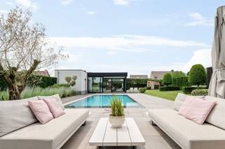 <p><span>Villa de luxe avec piscine et pool house à proximité du centre de Hoogstraten</span></p><p><span>Située dans un endroit calme mais central, à proximité du centre de Hoogstraten, cette spacieuse villa a été entièrement rénovée en 2019 pour offrir un état neuf. Cette demeure étonnamment spacieuse offre environ 425 m² de surface habitable !</span></p><p><span> </span></p><p><span>Agencement</span></p><p><span>Vous entrez dans la maison par le hall d'entrée, qui comprend des toilettes pour invités et un escalier menant à l'étage. Dès votre arrivée, une grande porte vitrée vous offre une vue dégagée sur le jardin. Depuis le hall d'entrée, vous accédez également à un espace bureau situé à l'avant de la maison. Le très spacieux espace de vie offre une vue magnifique sur le jardin et bénéficie d’une abondante lumière naturelle. Côté rue, il comprend une salle de jeux ou un deuxième bureau, un coin salon avec une cheminée à gaz, une salle à manger centrale et une cuisine ouverte dotée d’un grand îlot avec un coin petit-déjeuner. La cuisine bénéficie de finitions haut de gamme et est équipée de divers appareils encastrés. Depuis la cuisine, un passage mène à l’arrière-cuisine et à la buanderie, et permet d’accéder à la cave avec un espace de rangement supplémentaire.</span></p><p><span> </span></p><p><span>Étage</span></p><p><span>Un escalier moderne doté d’un éclairage indirect mène au couloir de nuit donnant accès à la spacieuse suite parentale composée d’une chambre, d’un dressing avec placards intégrés et d’une salle de bains spacieuse. On y trouve également deux chambres d’enfants très spacieuses avec placards intégrés et une deuxième salle de bains. Toutes les chambres sont équipées de volets roulants.</span></p><p><span> </span></p><p><span>Deuxième étage</span></p><p><span>Le deuxième étage a également été entièrement aménagé et fini ; il comprend un vaste espace polyvalent qui sert actuellement de bureau, ainsi qu’un grenier de rangement et un local technique.</span></p><p><span> </span></p><p><span>Sous-sol</span></p><p><span>Depuis l'arrière-cuisine, vous accédez au sous-sol qui vous offre un espace de rangement supplémentaire au frais.</span></p><p><span> </span></p><p><span>Pool house</span></p><p><span>Le pool house indépendant offre un espace multifonctionnel pouvant servir de salle de détente, de salle de fête ou de salle de sport. Il dispose de divers équipements, notamment une cuisine équipée avec divers appareils (lave-vaisselle, four, réfrigérateur avec congélateur), ainsi que des sanitaires avec douche et toilettes.</span></p><p><span> </span></p><p><span>Jardin, piscine et espaces extérieurs</span></p><p><span>Le magnifique jardin aménagé bénéficie d’une exposition sud et d’une grande intimité ; les spacieuses terrasses entourant la piscine chauffée offrent suffisamment d’espace pour installer des chaises longues et du mobilier de jardin. Au fond du jardin, un espace de jeux est prévu pour les enfants.</span></p><p><span> </span></p><p><span>Parking, garage et abri pour voiture</span></p><p><span>Des places de stationnement équipées d’une infrastructure de recharge pour véhicules électriques ont été prévues à côté et devant la villa. Il est possible d’aménager un garage intégré pouvant accueillir une voiture, ainsi qu’un abri de voiture sur le côté de la villa. Pour plus d’informations à ce sujet, veuillez contacter notre agence.</span></p><p><span> </span></p><p><span>Particularités</span></p><p><span>Cette spacieuse demeure est à la pointe de la technologie et a été entièrement rénovée en 2019 pour retrouver l’état d’une construction neuve. La villa est équipée d’un système domotique, d’un chauffage au sol avec pompe à chaleur (géothermie) ainsi que d’un système de refroidissement passif au rez-de-chaussée et au 1er étage. Puits foré, arrosage du jardin, jardin clôturé avec terrasses, piscine chauffée avec volet roulant automatique, pool house avec bar, cuisine, toilettes et douche. Système de ventilation, niveau E = 3 (maison BEN), panneaux solaires de 11 kW. Au premier étage, toutes les fenêtres sont équipées de volets roulants. Les fenêtres de la façade sud (façade arrière) ont été équipées de stores vénitiens, et un avant-toit a été aménagé pour profiter d'un ensoleillement optimal en fonction de la saison.</span></p><p><span> </span></p><p><span> </span></p>