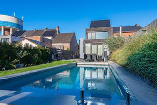 Hedendaagse driegevelwoning met prachtige tuin en zwemad. Zeer rustig en landelijk gelegen in een doodlopende straat nabij centrum, station en invalswegen. Recent (2017) en bijzonder lichtrijk, met kamerhoge ramen en open uitzicht over de zuidwest georiënteerde tuin. Voorzien van alle comfort, vloerverwarming, koeling, screens, elektrische rolluiken en zonnepanelen. Gelijkvloers met dubbele inkom, multifuncitonele ruimte van 42 m2 (praktijkruimte met gescheiden toegang mogelijk), toilet, berging en zeer mooie volledig ingerichte leefkeuken. Verdieping met living en dakterras, slaapkamer, badkamer met bad, inloopdouche en dubbele wastafel. Tweede verdieping met grote slaapkamer (29 m2) inclusief gedeeltelijk afgewerkte douchekamer. Uiterst verzorgde tuin met verwarmd zwembad, tuinhuis, serre en mooie natuur. Instapklaar. Een aanrader, uw bezoek waard.