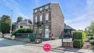 Deze statige, vrijstaande herenwoning ligt in de dorpskern van Eigenbilzen, vlak bij het Eigenbilzerplein en de Sint-Ursulakerk. De basisschool bevindt zich in het dorp. Ook winkels, het gezellige centrum en station van Bilzen en de verbindingswegen richting Maastricht, Genk en de E313 zijn vlot bereikbaar.<br /><br />De woning dateert van 1912 en staat op een zongericht perceel van 581 m². Ze omvat 208 m² bruikbare vloeroppervlakte en telt vier slaapkamers, aangevuld met verschillende praktische en multifunctionele ruimtes. Tussen 2019 en 2023 hebben de eigenaars de woning met veel liefde, kennis van haar geschiedenis en respect voor het oorspronkelijke karakter grondig gerenoveerd. Authentieke elementen werden daarbij zorgvuldig bewaard en gecombineerd met hedendaags wooncomfort en energiezuinige ingrepen.<br /><br />De markante bakstenen gevel met rondboogvensters, hardstenen accenten en sierbalkon geeft meteen aan dat dit geen alledaagse woning is. Ook het fraaie smeedijzeren voortuinhek draagt bij aan de uitstraling. Het zwart-wit geschilderde hekwerk dateert uit de eerste helft van de twintigste eeuw en is vanwege zijn erfgoedwaarde opgenomen in de Inventaris Onroerend Erfgoed. Verder is de woning vrijgesteld van deze inventaris. <br /><br />Binnen bleven eveneens verschillende kenmerkende elementen zichtbaar. Hoge plafonds, de originele parketvloeren, gerestaureerde binnendeuren en rijk uitgewerkte schouwmantels zorgen voor een warme, doorleefde uitstraling.<br /><br />Indeling<br /><br />Via de inkomhal met afzonderlijk gastentoilet bereik je de woonvertrekken. Aan de voorzijde ligt de woonkamer, waar de hoge plafonds van ca. 3,5 meter en de grote ramen voor een aangenaam ruimtegevoel en veel natuurlijke lichtinval zorgen. De sierlijke schouwmantel vormt hier een opvallend onderdeel van het interieur.<br /><br />Aansluitend bevindt zich de eetkamer met opnieuw een hoge plafondhoogte en een brede raampartij. De opeenvolging van woonkamer en eetkamer sluit aan bij de klassieke indeling van het pand en biedt tegelijk voldoende ruimte voor het dagelijkse gezinsleven.<br /><br />De keuken werd in 2023 volledig vernieuwd en sluit qua vormgeving mooi aan bij de stijl van de woning. Donkere kastfronten, een houten werkblad, messingkleurig beslag en een opvallende fornuisombouw met decoratieve reliëftegels vormen samen een bijzonder geheel. De keuken is uitgerust met een keramische kookplaat, een koelkast met diepvriesgedeelte, een vaatwasser en een afzonderlijke oven en microgolfoven.<br /><br />Achteraan bevindt zich de royale glazen tuinkamer. Het glazen dak en de brede schuifpartijen laten veel daglicht binnen en zorgen voor een rechtstreekse verbinding met de tuin. De oorspronkelijke bakstenen achtergevel bleef hier zichtbaar en vormt een karaktervolle achtergrond. Deze ruimte is voorzien van verwarming en kan het hele jaar door gebruikt worden als eetplaats, tweede zithoek of plek om rustig van de tuin te genieten.<br /><br />Verder beschikt het gelijkvloers over een praktische berging en een afzonderlijk ingerichte wasruimte met plaats voor huishoudtoestellen en voorraad.<br /><br />Op de eerste verdieping leidt de overloop naar twee slaapkamers. Ook hier zorgen de hoge ramen, houten vloeren en aanwezige schouwmantels voor een sfeer die veel weg heeft van een boutique-hotel. De badkamer werd in 2022 volledig vernieuwd en is ingericht met een ruime inloopdouche, een badkamermeubel met lavabo en een toilet. De witte afwerking, glazen kroonluchter en blauw getinte decoratieve tegels geven de ruimte een frisse, verzorgde uitstraling.<br /><br />Een vaste trap brengt je naar de ingerichte bovenverdieping. Hier bevinden zich twee bijkomende kamers, waardoor de woning in totaal vier slaapkamers telt. Afhankelijk van de behoefte kunnen deze ruimtes ook worden ingericht als bureau, hobbykamer, logeerkamer of extra leefruimte.<br /><br />Vooral de open ruimte onder het dak is bijzonder. Het hoge plafond, het vrijgelegde houten gebinte en de zichtbaar gehouden delen van de baksteenstructuur geven deze verdieping een uitgesproken karakter. De authentieke materialen maken de geschiedenis van het pand tastbaar, terwijl de eigentijdse afwerking voor een persoonlijke en comfortabele woonomgeving zorgt. <br /><br />De kelder van circa 25 m² biedt bijkomende plaats voor voorraad en de technische installatie.<br /><br />Ook buiten werd de woning verzorgd aangepakt. De glazen tuinkamer opent volledig naar het terras en de tuin. De bestrating en volwassen groene omkadering zorgen voor een aangename buitenruimte met de nodige privacy. Aan de zijkant bevindt zich een brede oprit en voor de woning zijn twee parkeerplaatsen beschikbaar. Als kers op de taart wordt de oprit nog afgewerkt met een toegangspoort. <br /><br />Ook technisch werden belangrijke investeringen uitgevoerd. De elektrische installatie, riolering, waterleidingen, verwarmingsleidingen en radiatoren werden vernieuwd. De woning beschikt over een condenserende gasketel van ATAG, een waterontharder en pvc- en aluminium buitenschrijnwerk met hoogrendementsbeglazing. Daarnaast werden het dak, de muren en een groot deel van de vloeren geïsoleerd. Deze ingrepen resulteren in een EPC-label C met een energiescore van 278 kWh/(m² jaar).<br /><br />Belangrijkste troeven:<br /><br />- Statige, vrijstaande herenwoning uit 1912<br />- Gelegen in de dorpskern, vlak bij het Eigenbilzerplein<br />- 208 m² bruikbare vloeroppervlakte volgens het EPC<br />- Vier slaapkamers en verschillende multifunctionele ruimtes<br />- Grondige totaalrenovatie uitgevoerd tussen 2019 en 2023<br />- Met liefde en respect voor het oorspronkelijke karakter gerenoveerd<br />- Hoge plafonds, houten vloeren en rijk uitgewerkte schouwmantels<br />- Vrijgelegd houten gebinte en zichtbaar baksteenwerk<br />- Historisch smeedijzeren voortuinhek met erfgoedwaarde<br />- Vernieuwde keuken met een uitgesproken, karaktervolle afwerking<br />- Royale glazen tuinkamer met brede schuifpartijen<br />- Vernieuwde badkamer en praktische wasruimte<br />- Vernieuwde technieken en doorgedreven isolatiewerken<br />- EPC-label C<br />- Zongericht perceel van 581 m²<br /><br />Deze woning richt zich tot wie houdt van een pand met geschiedenis, ruimte en een uitgesproken eigen karakter, zonder afstand te willen doen van hedendaags wooncomfort.<br /><br />Wil je deze bijzondere herenwoning zelf ontdekken? Neem contact op met Immofair via 089 390 990 of info@immofair.be voor meer informatie of een persoonlijke bezichtiging.