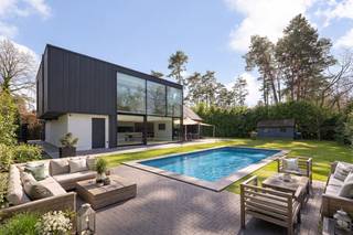 <p>In een rustige, residentiële villawijk bevindt zich deze uitzonderlijke, instapklare villa waar design, comfort en licht centraal staan. Achter de strakke gevel schuilt een verrassend ruime woning met een warme, minimalistische afwerking en hoogwaardige materialen.<br /><br />Grote raampartijen en een doordachte architectuur zorgen doorheen de hele woning voor een unieke beleving van licht en ruimte.<br /><br /><span><strong>INDELING</strong></span><br /><br />U wordt verwelkomd in een imposante inkomhal met vide en maatkasten. Via stijlvolle glazen pivotdeuren bereikt u de lichtrijke leefruimte met gezellige zithoek en ingewerkte haard.<br /><br />De open leefkeuken met strak kookeiland en kwalitatieve toestellen sluit naadloos aan op de eetruimte, die dankzij grote raampartijen uitkijkt op de tuin en het zwembad.<br /><br />Op de verdieping bevinden zich meerdere ruime slaapkamers (5 in totaal). De master suite beschikt over ingemaakte kasten en een luxueuze badkamer met vrijstaand bad, inloopdouche en dubbele wastafel.<br /><br />Daarnaast is er nog een extra badkamer aanwezig.<br /><br /><span><strong>BIJZONDERHEDEN</strong></span><br /><br />- Architecturale villa met overvloed aan natuurlijk licht<br />- Grote raampartijen met directe connectie naar tuin en terras<br />- Zwembad en sauna aanwezig<br />- Inpandige garage en praktische bergruimtes<br />- Airconditioning en moderne technieken aanwezig<br />- Mogelijkheid tot het inrichten van een kantoor of praktijkruimte op het gelijkvloers<br /><br />Een unieke kans voor wie op zoek is naar exclusief wonen met een perfecte balans tussen luxe en functionaliteit.</p>