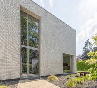 <h3>Exclusieve architectenvilla op toplocatie in villawijk De Lint</h3>
<p>Op een prachtig zuidwestgericht perceel, op wandelafstand van het unieke natuurgebied De Liereman, bevindt zich deze hedendaagse en onder architectuur gebouwde villa. Deze uitzonderlijke woning combineert tijdloze architectuur, royale leefruimtes en een hoogwaardig afwerkingsniveau met een uitstekende bereikbaarheid. Zowel Eindhoven als Antwerpen bevinden zich op slechts ca. 25 minuten rijden, waardoor u geniet van het beste van twee werelden: rust, natuur en een vlotte verbinding.</p>
<p>Bij aankomst wordt u verwelkomd in een ruime inkomhal met vestiaire en gastentoilet. Via stijlvolle dubbele deuren betreedt u de indrukwekkende woonkamer, waar de grote raampartijen een panoramisch zicht bieden op de prachtig aangelegde tuin. Het overvloedige natuurlijke licht en de fraaie tuinzichten creëren een unieke woonbeleving. Aansluitend bevindt zich een open ruimte die perfect dienst kan doen als bureau of leeshoek, open van karakter maar toch afzonderlijk van de leefruimte.</p>
<p>De sfeervolle doorkijkhaard vormt een elegante verbinding tussen de woonkamer en de royale leefkeuken. Deze keuken verkeert in perfecte staat van onderhoud, is uitgerust met kwalitatieve toestellen, beschikt over een groot werkblad en biedt plaats aan een ruime eettafel. Dankzij de grote schuiframen loopt binnen naadloos over in buiten. Achter de keuken bevinden zich een praktische bijkeuken en een aparte wasruimte. De inpandige dubbele garage met automatische poort en personenlift vervolledigt het comfort op het gelijkvloers.</p>
<p>Op de verdieping geeft de royale nachthal toegang tot de indrukwekkende master suite met inloopdressing en een luxueuze badkamer. Daarnaast zijn er nog twee volwaardige slaapkamers met een gedeelde badkamer. De ruime studiekamer kan eenvoudig worden ingericht als vierde slaapkamer en beschikt bovendien over een eigen terras.</p>
<p>Ook buiten weet deze villa te imponeren. De volgroeide, volledig omheinde tuin biedt optimale privacy en vormt een waar groen paradijs. Meerdere zonneterrassen en een overdekt terras nodigen uit om in alle seizoenen van het buitenleven te genieten. Het extra losstaande garagegebouw biedt bijkomende mogelijkheden voor wagenliefhebbers, hobbyruimte of extra opslag.</p>
<p>Naast het uitzonderlijke wooncomfort onderscheidt deze villa zich door haar onderhoudsvriendelijke karakter. Dankzij de duurzame aluminium raamprofielen en de kwalitatieve gevels in gevelsteen zijn er geen schilderwerken aan het buitenschrijnwerk of de buitenmuren nodig, wat resulteert in een stijlvolle uitstraling met een minimum aan onderhoud.<br /><br /><strong>Een uitzonderlijke villa voor wie ruimte, comfort, privacy, kwaliteit en een onderhoudsarme woonomgeving weet te waarderen.</strong></p>
<h3>Troeven van deze woning</h3>
<ul>
<li>Wandelafstand van natuurgebied De Liereman</li>
<li>Zuidwestgericht perceel met optimale bezonning</li>
<li>Personenlift naar de verdieping</li>
<li>Vloerverwarming op gelijkvloers én verdieping</li>
<li>Inpandige dubbele garage met automatische poort</li>
<li>Extra losstaand garagegebouw met bergzolder</li>
<li>Alarmsysteem</li>
<li>Zonnescreens</li>
<li>Fraai aangelegde, volledig omheinde tuin</li>
<li>Grote terrassen en overdekt, verwarmd terras</li>
</ul>