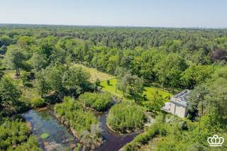 <p><span>Uitzonderlijk landgoed met luxueuze villa en stijlvolle oranjerie in het Mastenbos</span></p><p><span> </span></p><p><span>Op een steenworp van het dorpscentrum van Kapellen, gelegen in het Mastenbos, bevindt zich dit uitzonderlijke en bijzonder sfeervolle domein van meer dan 2 hectare. Het voormalige koetshuis en de authentieke oranjerie van het historische Kasteel Mastenhof werden met bijzonder veel respect voor hun karakter en architectuur gerenoveerd en vormen vandaag een uniek geheel waar historische charme, hedendaags comfort en natuur harmonieus samenkomen.</span></p><p><span> </span></p><p><span>Koetshuis / Villa</span></p><p><span>Het voormalige koetshuis werd getransformeerd tot een luxueuze villa met een uitgesproken karakter en warme uitstraling. De villa beschikt over maar liefst 6 slaapkamers en 3 badkamers. De leefruimtes omvatten een ruime zitkamer, een sfeervolle eetkamer, een bureau en een royale leefkeuken die als het kloppende hart van de woning fungeert. Vanuit de leefkeuken is er rechtstreeks toegang tot de bijzonder charmante, fraai aangelegde binnentuin met verschillende terrassen. </span></p><p><span>Authentieke architecturale elementen werden zorgvuldig behouden en gecombineerd met hedendaags wooncomfort, waardoor de villa een unieke sfeer en tijdloze uitstraling heeft. De aanwezige wellnessvoorzieningen vervolledigen het gevoel van comfort en exclusiviteit.</span></p><p><span> </span></p><p><span>Oranjerie</span></p><p><span>Als tweede volwaardige woonentiteit beschikt het domein over een prachtig gerenoveerde oranjerie. Deze karaktervolle ruimte omvat een royale leefruimte met open haard, een afzonderlijke en moderne keuken en op de verdieping een luxueuze suite met slaapkamer, dressing en ensuite badkamer.</span></p><p><span>De suite bevindt zich onder een indrukwekkend glazen dak en baadt in natuurlijk licht. Dankzij de grote raampartijen en openslaande deuren wordt een voortdurende verbinding met de tuin gecreëerd en geniet men van een weids en bijzonder fraai uitzicht over het omliggende groen. De oranjerie leent zich dan ook uitstekend als stijlvol gastenverblijf, tweede woonunit of inspirerende werk- en ontvangstruimte.</span></p><p><span> </span></p><p><span>Tuin</span></p><p><span>Ook het domein zelf is van een zeldzame kwaliteit, aangelegd in een typische Engelse stijl. De waardevolle natuur vormt een prachtig en gevarieerd geheel van bossen, weilanden en natuurlijke waterpartijen, waardoor privacy, rust en een sterk gevoel van ruimte gegarandeerd zijn.</span></p>