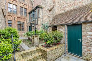 In het hart van Brugge, verscholen achter een discreet muurtje met toegangspoort, bevindt zich dit uitzonderlijke gotische herenhuis uit 1550. Een bijzonder stukje Brugs erfgoed, met één van de slechts twee bewaarde originele houten gevels in de stad. Authentiek, karaktervol en bovenal uniek.<br /><br />De ligging is al even bijzonder als het pand zelf. Vanuit de Vlamingstraat wandelt u zo naar het Belfort, de Markt en de vele restaurants, boetieks en culturele trekpleisters die de Brugse binnenstad rijk is. Een uitzonderlijke locatie voor wie volop van het stadsleven wil genieten en tegelijk waarde hecht aan privacy en rust.<br /><br />Binnen zet de historische grandeur zich moeiteloos voort. Robuuste houten plafondbalken, fraaie parketvloeren, authentieke muurnissen en een sfeervolle open haard geven de woonvertrekken een warme en tijdloze uitstraling.<br /><br />De woning omvat een eetruimte met keuken, een karaktervolle salon met open haard, twee slaapkamers met de mogelijkheid om een derde slaapkamer te creëren, en een badkamer, verdeeld over het gelijkvloers en twee verdiepingen.<br /><br />Wie historisch karakter graag combineert met hedendaags wooncomfort, vindt hier bovendien heel wat mogelijkheden. Zo kan de bestaande keuken worden omgevormd tot een moderne open keuken door onder meer het lage tussenmuurtje weg te nemen. Ook de badkamer kan volledig worden vernieuwd tot een eigentijdse badkamer met douche, lavabo en toilet. Rond de karaktervolle eiken spiltrap kan bovendien een stijlvolle stalen leuning worden geplaatst, als hedendaags accent dat mooi contrasteert met de authentieke elementen van de woning.<br />Een absolute blikvanger is de prachtige erker op de eerste verdieping, vanwaar u uitkijkt over de charmant aangelegde binnentuin.<br /><br />Ook ondergronds verrast deze woning. De ruime middeleeuwse kelder biedt tal van mogelijkheden en vormt opnieuw een bijzonder authentiek onderdeel van het geheel.<br />Buiten vormt de beschutte binnentuin een groene oase midden in de stad. Hier geniet u in alle privacy van rust, groen en de unieke sfeer van een eeuwenoud Brugs herenhuis.<br /><br />Een zeldzame stadsparel voor wie op zoek is naar méér dan een woning: beschermd erfgoed, een uitzonderlijke houten gevel te Kortewinkel, een authentiek interieur en een topligging komen hier samen in een eigendom met een werkelijk uniek karakter.