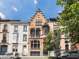ETTERBEEK – Tussen de Chasse en de Avenue de la Couronne, in een van de veiligste straten van Etterbeek dankzij de nabijheid van de kazerne en het gemeentehuis van Etterbeek, staat een huis dat in 1912 door architect Augustin Goovaerts in neogotische stijl werd gebouwd. Dit huis met een bewoonbare oppervlakte van ±435 m² wordt gekenmerkt door zijn architectuur en zijn halve toren die vanaf de straatkant zichtbaar is.<br /><br /><span>Bovenste begane grond:</span><br /><br />3 aaneengesloten woonruimtes van respectievelijk ± 19 m², 20 m² en de bibliotheek over 2 verdiepingen van elk ± 25,5 m², elk met hun historische kenmerken zoals originele wandtapijten en antieke schouwen; de bibliotheek heeft ook toegang tot 2 kantoren en de tuin.<br /><br /><span>Benedenverdieping:</span><br /><br />2 ruime multifunctionele kamers van ± 17 m² en ± 15 m² en achterin een grote ingerichte keuken met toegang tot de tuin.<br /><br /><span>1e verdieping: </span><br />
<ul>
<li>2 slaapkamers van ± 19 m² en ± 21 m²</li>
<li>Toilet</li>
<li>Kleedruimte van ± 7,5 m²</li>
<li>Badkamer van ± 9 m²</li>
</ul>
<span>2e verdieping:</span><br />
<ul>
<li>Een slaapkamer van ±16 m²</li>
<li>De ouderslaapkamer van ±18 m² met eigen doucheruimte, wastafel en een ingebouwde kleedkamer</li>
<li>Een gemeenschappelijke badkamer met toilet van ±10 m²</li>
<li>Een kleedruimte van ±9,5 m²</li>
</ul>
Op de bovenste verdieping bevindt zich een inrichtbare zolder van ± 34 m²<br />Verschillende ruimtes onder de trap bieden extra opbergruimte. Er zijn ook kelders, waaronder een wijnkelder. Het huis is voorzien van een intercom en glasvezel.