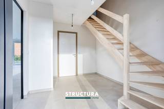 Deze kwalitatief afgewerkte nieuwbouwwoning combineert een centrale en rustige ligging in Mazenzele met een ruime indeling en hedendaags wooncomfort. De open bebouwing bevindt zich op een perceel van 5a 54ca en beschikt over vier slaapkamers, twee badkamers en een ruime inpandige garage. De zuidgerichte leefruimte en het aansluitende terras maken het hier aangenaam wonen, zowel binnen als buiten. Op het gelijkvloers verwelkomt de inkomhal met vestiaire en afzonderlijk gastentoilet u. De ruime leef- en eetruimte vormt samen met de kwalitatief uitgeruste open keuken met eiland het hart van de woning. Aansluitend geniet u van het terras en de mooie tuin, waar u in alle rust kunt ontspannen. De zeer ruime inpandige garage met aansluitende bergruimte vervolledigen deze verdieping.De eerste verdieping telt vier slaapkamers en twee badkamers. De grote badkamer is uitgerust met een ligbad en een douche; de tweede badkamer beschikt over een douchecel. Daarnaast bevinden zich hier een afzonderlijk toilet en een bijkomende berging. De geïsoleerde zolder biedt nog eens circa 40 m² handige opbergruimte.Ook op technisch vlak is deze woning bijzonder compleet. Met een E-peil van 5, zonnepanelen en een lucht-waterwarmtepomp met vloerverwarming en koelmodule staat energiezuinig wooncomfort centraal. Het ventilatiesysteem D (met hygrofunctie) draagt bij aan een aangenaam binnenklimaat. Verder beschikt de woning over een regenwaterput van 10.000 liter en een voorziening voor de installatie van een laadpaal.Een ruime nieuwbouwwoning voor wie rustig wil wonen in Mazenzele, met alle comfort en aandacht voor energiezuinigheid.De verkoop geschiedt met toepassing van btw op de constructiewaarde.Interesse? Contacteer Structura voor meer informatie of een bezoek ter plaatse op 02/460.80.46 of info@structura.be