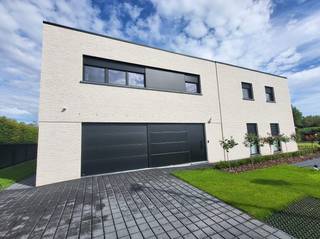 Instapklare nieuwbouwwoning (2025) op perceel van 1.167 m²<br />Op zoek naar een recent gebouwde woning die alles biedt wat een hedendaags gezin nodig heeft ?<br />Met een voorgevelbreedte van maar liefst 18 meter straalt deze eigendom ruimte en elegantie uit. Bij het betreden van de woning verwelkomt de stijlvolle inkomhal met gastentoilet u in een moderne leefomgeving. Via een doorgang met maatwerkkasten bereikt u de royale leefruimte waar woonkamer, eetplaats en open keuken naadloos in elkaar overvloeien. <br />De moderne keuken beschikt over een overvloed aan kastruimte en vormt het hart van de woning. Dankzij het grote schuifraam is de directe verbinding met het overdekte terras en de tuin. Aansluitend bevindt zich een praktische berging/wasplaats met afzonderlijke buitendeur.<br />Het gelijkvloers biedt daarnaast een comfortabele slaapkamer met dressing en een ruime badkamer met een ligbad als een stijlvolle inloopdouche. Ook de ruime garage met sectionaalpoort zorgt voor extra comfort en praktische opbergruimte.<br />Op de verdieping bevinden zich nog een tweede badkamer, een extra slaapkamer en twee volwaardige kamers. Hierdoor is deze woning uitermate geschikt voor grotere gezinnen of voor wie een thuisbureau of hobbyruimte wenst te creëren.<br />Buiten geniet u van een volledig aangelegde en omheinde tuin met een ruim tuinhuis van 25 m² en een overkapping van 15 m², beide voorzien van een tegelvloer. De automatische schuifpoort (4 m x 1,80 m) zorgt voor extra veiligheid en gebruiksgemak.<br />Ook op technisch vlak laat deze woning niets te wensen over. Ze is uitgerust met zonnepanelen, energiezuinige vloerverwarming, ventilatiesysteem D, elektrische rolluiken, domotica en een regenwaterrecuperatiesysteem.<br />Een bijkomende troef zijn de extra brede binnendeuren, die niet alleen een gevoel van ruimte creëren maar ook het wooncomfort verhogen voor minder mobiele bewoners.<br />Laat u verrassen door de ruimte, de afwerking en het wooncomfort van deze bijzondere eigendom.<br />bijkomende info 0477/241084.<br />