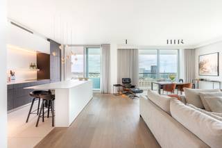 <p>Stijlvol appartement gelegen op het Eilandje, in het iconische Chipperfield-project, met spectaculair zicht. Gelegen op de 13e verdieping van een residentie met 15 verdiepingen, geniet u hier van een uitzonderlijk panoramisch uitzicht over de stad, de haven en het water.</p>
<p>Een brede, lichtrijke inkomhal biedt toegang tot alle kamers en leidt naadloos naar een ruime leefruimte. Een hoogwaardige Bulthaupt-keuken is voorzien van Miele-apparatuur, inclusief stoom- en grilloven. De leefruimte, met 3,2 meter hoge plafonds, is afgewerkt met een warme parketvloer en beschikt over ingemaakt kastenwerk met bar en een elegante ethanolhaard. Dankzij de kamerhoge raampartijen en meerdere glazen schuifpuien geniet u vanuit elke hoek van een adembenemend panorama over het Kattendijkdok en de Antwerpse skyline.</p>
<p>Vanuit alle kamers heeft u toegang tot het zuidgerichte omloop-hoekterras, één van de unieke troeven van dit appartement. Op deze hoogte geniet u ongestoord van het water, de stad en de haven — met een glazen balustrade die het zicht maximaal vrijlaat.</p>
<p>Verder beschikt het appartement over een master-slaapkamer met ensuite badkamer voorzien van inloopdouche, dubbele wastafel en toilet, afgewerkt in Corian. De oorspronkelijke tweede doucheruimte werd omgebouwd tot een praktische wasplaats (volledig ingericht, maar eenvoudig opnieuw als douchekamer te gebruiken). Daarnaast is er een tweede kamer ingericht als bureau met ingebouwde kasten en een geïntegreerd stapelbed, waardoor deze ook perfect kan functioneren als volwaardige tweede slaapkamer.<br /><br /><strong>De twee ondergrondse autostaanplaatsen kunnen aangekocht worden voor € 80.000; de kelderberging is inbegrepen.</strong></p>
<p>Een zeldzame kans om te wonen op één van de meest exclusieve locaties van Antwerpen, hoog boven de stad, in één van de meest gegeerde en dynamische buurten waar erfgoed en hedendaagse architectuur elkaar ontmoeten. Op wandelafstand van het MAS, sfeervolle terrassen aan het water, toprestaurants, boetieks en uitstekende verbindingen met de rest van de stad.</p>