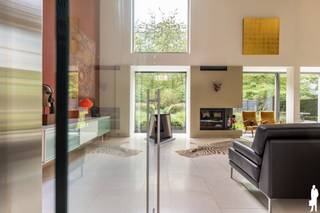 <p><strong>Exclusieve architectenwoning met panoramisch zicht op natuurgebied<br /></strong>Aan de rand van Park Callebeek-Terlocht, met toegang vanuit de eigen tuin, bevindt zich deze bijzondere architectenwoning. Qua ligging en bereikbaarheid in de onmiddellijk nabijheid van de waterbus, welke rechtstreeks en file-vrij een unieke regelmatige verbinding geeft met het centrum van Antwerpen.<br /><br />Met <strong>ca. 570 m² bew. opp.,</strong> een doordachte indeling en een sterke architecturale uitstraling combineert de woning comfortabel wonen met de mogelijkheid om een professionele activiteit uit te oefenen. Hoge plafonds, grote glaspartijen, maatwerk en zorgvuldig gekozen materialen bepalen het karakter. Het ontwerp verscheen bovendien in verschillende architectuur- en interieurpublicaties.<br /><br /><strong>Wonen met zicht op groen<br /></strong>Via de ruime inkomhal met <strong>lift</strong> bereikt u de leefruimte met vide. De hoge plafonds en grote raampartijen zorgen voor veel licht en een open zicht op de tuin. Een sfeervolle haard brengt warmte in het strakke interieur.<br /><br />De aansluitende maatwerkkeuken beschikt over een groot kookeiland, hoogwaardige toestellen en een geïntegreerde eetruimte. Donkere houtaccenten en lichte materialen vormen er een stijlvol geheel.<br /><br />Op het GLVL bevinden zich verder een bijkeuken/wasplaats, een multifunctionele ruimte die ook als logeerkamer kan dienen, met douchevoorziening, en een dubbele inpandige garage.<br /><br /><strong>Rust en privacy op de eerste verdieping<br /></strong>De 1eV herbergt een royale master suite met dressing en luxueuze badkamer, inclusief hamam. Daarnaast bevindt zich een bijzonder ruime tweede slaapkamer met eigen douchekamer, eventueel op te delen in twee afzonderlijke slaapkamers.<br /><br />Een <strong>open home office</strong> met zicht op de onderliggende leefruimte en de groene omgeving vervolledigt deze verdieping.<br /><br /><strong>Een veelzijdige tweede verdieping<br /></strong>De 2eV, met een opp. van ca. 140 m², is ingericht als<strong> professionele kantoorruimte </strong>en biedt uitzonderlijke mogelijkheden.<br /><br />De oorspronkelijke stedenbouwkundige vergunning voorziet in een combinatie van wonen en een praktijk voor een vrij beroep. Dit maakt de woning interessant voor wie wonen en werken op een stijlvolle manier wil verenigen. Ook andere invullingen als creatieve studio of bijkomende privéruimte (kangoeroewonen) bieden perspectieven, onder voorbehoud van de geldende voorschriften.<br /><br />Absolute blikvanger is het <strong>royale terras van ca. 47 m²</strong>, met een adembenemend uitzicht over het aangrenzende natuurgebied.<br /><br />Een volledig beglaasde panoramaruimte op het hoogste niveau vormt de architecturale bekroning van deze residentie.<br /><br /><strong>Een tuin die aansluit op het landschap<br /></strong>De aangelegde tuin met siergrassen, volwassen bomen en strakke lijnen vormt een rustig verlengde van de woning. Via de tuin heeft u rechtstreeks toegang tot het achterliggende park: een bijzondere meerwaarde voor wie graag midden in het groen woont.<br /><br /><strong>Comfort en techniek<br /></strong>De lift verbindt de kelder met de 2eV. Verder beschikt de woning over zonnepanelen, zonnecollectoren, airco, automatische zonwering, uitgebreide veiligheidsvoorzieningen en talrijke ingemaakte kasten. De ruime kelder biedt plaats voor opslag, archief of een wijncollectie.<br /><br /><strong>Bijzondere troeven:</strong></p>
<ul>
<li>Ca. 570 m² bew. opp.</li>
<li>Rechtstreekse toegang tot Park Callebeek-Terlocht</li>
<li>Lichtrijke leefruimte met vide</li>
<li>Master suite met dressing</li>
<li>2eV van ca. 140 m² met veel mogelijkheden, bereikbaar met lift</li>
<li>Panoramisch terras van ca. 47 m²</li>
<li>Dubbele garage en extra parkeergelegenheid</li>
<li>EPC B – 123 kWh/m²</li>
<li>Zonnepanelen, zonnecollectoren en warmtepompen</li>
<li>Veel ingemaakte kasten en automatische zonwering</li>
</ul>