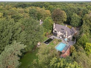 <p>Verscholen tussen eeuwenoude bomen aan één van de gegeerde dreven in Schilde ligt deze indrukwekkende villa die pure klasse, ruimte en privacy ademt. <br />De baksteengevel met glooiende leien daken, sierlijke schoorstenen en vakwerkdetails in combinatie met een kasseien oprit, omzoomd door strak geschoren hagen, een zeldzame combinatie van authentieke allure en hedendaags comfort.</p>
<p>De inkomhal met blauwe natuursteen vormt het hart van de woning en geeft toegang tot de verschillende woonvertrekken. <br />De lichte woonkamer met gashaard vloeit naadloos over in de eetkamer en de ruime keuken, waardoor een prachtige open leefruimte ontstaat met fraai zicht op de tuin. De leefkeuken is uitgewerkt met een eiland afgewerkt met blauwe natuurstenen werkblad. Een professioneel Viking gasfornuis aangevuld met premium toestellen zorgt voor extra comfort. De gashaard creërt warmte en gezelligheid bij het diner. <br />Overal in de villa is hoogwaardig houten maatwerk verwerkt. De vloeren zijn zorgvuldig gekozen: blauwe natuursteen in de inkom en keuken, warm eiken parket in de overige ruimtes. Een wijnkelder maakt het plaatje compleet. Alle leefruimtes zijn voorzien van vloerverwarming en airconditioning.</p>
<p>Op de eerste verdieping geniet u van een royale mastersuite met dressing, slaapgedeelte en een luxe badkamer met inloopdouche, ligbad en dubbele wastafel. Daarnaast vindt u een tweede slaapkamer met eigen badkamer, twee extra slaapkamers en een derde badkamer. Alle slaapkamers zijn uitgerust met airconditioning. <br />De bovenste verdieping herbergt een comfortabel gastenvertrek met eigen badkamer.</p>
<p>Buiten opent zich een weelderige tuin. Achteraan aan het zonneterras grenst een verwarmd zwembad met poolhouse, compleet met wellnessvoorzieningen (sauna, stoombad en douche) en een Silverspa-jacuzzi voor zes personen. Een tweede bijhuis fungeert als sfeervol clubhouse. De grote koivijver vormt een rustgevend middelpunt in de tuin. <br />Twee inpandige garages en ruim voldoende parkeergelegenheid buiten vervolmaken het geheel.<br />Deze villa biedt een exclusieve leefomgeving waar rust, luxe en genieten samenkomen.</p>