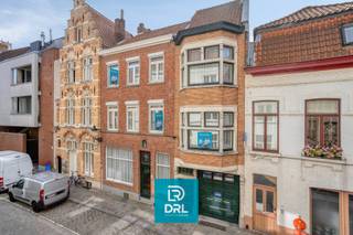 Op een <strong>absolute topligging in het historische centrum van Brugge</strong>, vlak bij het Simon Stevinplein en op wandelafstand van de Markt, bieden wij een bijzonder vastgoedensemble aan met een zelden geziene combinatie van <strong>ruimte, karakter, comfort en mogelijkheden</strong>.<br />Het geheel bestaat uit <strong>vier onroerende goederen</strong>: <strong>Zilverstraat 17</strong>, <strong>Zilverstraat 19</strong>, het woongedeelte van <strong>Steenstraat 56</strong> <em>(exclusief het handelsgelijkvloers)</em> en een <strong>overdekte staanplaats voor twee wagens in de Kopstraat</strong>.<br />De verschillende eigendommen vormen samen een uitzonderlijk geheel en bieden tal van mogelijkheden voor <strong>wonen en werken onder één dak, vrije beroepen, kantoor of praktijk, atelier, een ruime stadsresidentie of een combinatie hiervan</strong>.<br />Een absolute blikvanger is bovendien het <strong>fantastische uitzicht over de historische binnenstad, het Simon Stevinplein en de drie iconische Brugse torens</strong>.<br /><br /><u>Zilverstraat 17</u><br />Achter de brede, karaktervolle gevel gaat een verrassend ruim pand schuil.<br />Op het gelijkvloers bevinden zich een <strong>bureau-/praktijkruimte</strong>, toilet en een bijzondere multifunctionele ruimte waarin zich een <strong>binnenzwembad</strong> bevindt. Het zwembad is momenteel volledig afgedekt met een houten vloer, waardoor deze ruimte vandaag perfect als hobby- of ontspanningsruimte kan worden gebruikt. De oorspronkelijke zwembadfunctie kan opnieuw zichtbaar worden gemaakt.<br />Via de traphal bereikt men de bovenliggende woonvertrekken met onder meer een <strong>leefruimte, keuken en terras</strong>, gevolgd door een nachthal, slaapkamer en badkamer.<br /><br /><u>Zilverstraat 19</u><br />Het naastgelegen pand is onmiddellijk herkenbaar aan zijn karakteristieke <strong>vooruitstekende gevel</strong> en vormt mee de verbinding tussen de verschillende delen van het vastgoedensemble.<br />Het omvat onder meer een <strong>inkomhal, inpandige garage, kelder, toilet, twee bergingen, keuken en achterplaats</strong>.<br />Vanuit dit gedeelte is er via <strong>trap én lift</strong> verbinding met de bovenliggende verdiepingen en met Steenstraat 56.<br />De verdiepingen omvatten onder meer een <strong>bureau-/atelierruimte met toilet</strong>, meerdere kamers, verschillende badkamers, toiletten en een terrasje. Ook de zolderverdieping werd ingericht met bijkomende kamers en sanitair.<br /><br /><u>Steenstraat 56</u><br />Aan de zijde van de Steenstraat bevindt zich een bijzonder karaktervol historisch pand met een prachtige trapgevel.<br /><strong>Het handelsgelijkvloers behoort niet tot het aangeboden vastgoed.</strong><br />Het woongedeelte omvat onder meer een <strong>leefruimte, salon/zitplaats, keuken, veranda, bureau, berging en toilet</strong>. Op de verdieping bevinden zich <strong>twee slaapkamers, een badkamer en terras</strong>, aangevuld met een zolderruimte.<br />Vanuit de hoger gelegen ruimtes geniet men van prachtige vergezichten over de Brugse binnenstad en zijn monumentale skyline.<br /><br />Ondanks het uitgesproken historische karakter beschikt het geheel over verschillende hedendaagse comfortelementen. Zo zijn er <strong>diverse airconditioningstoestellen</strong> aanwezig en zorgt de <strong>lift</strong> voor extra comfort en een praktische verbinding tussen verschillende niveaus van het complex. De combinatie met het binnenzwembad, terrassen en buitenruimtes maakt het geheel des te uitzonderlijker.<br /><br />Een niet te onderschatten troef in het centrum van Brugge is de aanwezigheid van een <strong>overdekte staanplaats voor twee wagens in de Kopstraat</strong>. Samen met de garage in Zilverstraat 19 betekent dit een bijzonder waardevolle parkeerfaciliteit op een locatie waar private parkeermogelijkheden uiterst schaars zijn.<br /><br />Dit is geen klassieke stadswoning, maar een <strong>uniek en veelzijdig vastgoedensemble</strong> met verschillende adressen en toegangen, royale volumes, garage, lift, zwembad, terrassen, werk- en praktijkruimtes en parkeerplaats voor twee wagens.<br /><br />Meer info of een bezoek inplannen, bel of mail DRL VASTGOED, 050 65 95 95 of info@drlvastgoed.be<br />