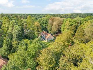Op een discreet perceel treffen we deze karaktervolle villa in landelijke architectuur. De woning is omgeven door een volwassen tuin met imposante bomen en geniet hierdoor van een aangename privacy.<br /><br />Binnen valt meteen het warme karakter van de woning op. De royale leefruimte wordt gekenmerkt door zichtbare houten balken, een terracottavloer, een natuurstenen open haard en talrijke raampartijen die voor veel natuurlijk licht en een mooie verbinding met de tuin zorgen. De hedendaagse leefkeuken vormt samen met de afzonderlijke ontbijthoek een aangename dagelijkse leefplek. Met 3 a 4 slaapkamers, twee badkamers, een ruim bureau, een inpandige garage en een volwaardige master suite biedt deze woning bovendien een bijzonder comfortabele gezinsindeling.<br /><br />Indeling gelijkvloers:<br />De inkomhal geeft toegang tot de verschillende vertrekken op het gelijkvloers. Een afzonderlijk en lichtrijk bureau, voorzien van brede raampartijen met zicht op het groen, biedt een aangename thuiswerkplek en kan tevens polyvalent worden ingericht.<br /><br />Centraal in de woning bevindt zich de ruime leefkamer met zit- en eetgedeelte. De houten balkenstructuur, terracottavloer en natuurstenen open haard zorgen hier voor een warme en karaktervolle uitstraling. Grote ramen en tuindeuren versterken het contact met de omliggende tuin. De open trap en vide geven het geheel bovendien een aangenaam gevoel van ruimte.<br /><br />De leefkeuken werd hedendaags ingericht met een royaal centraal kookeiland, veel kastruimte en kwalitatieve toestellen. Aansluitend bevindt zich een afzonderlijke ontbijthoek met veel natuurlijke lichtinval.<br /><br />Verder beschikt het gelijkvloers over een inpandige garage die eveneens plaats biedt aan de wasvoorzieningen en bijkomende bergruimte.<br /><br />Eerste verdieping:<br />De eerste verdieping omvat een volwaardig slaapgedeelte met in totaal 3 slaapkamers en een dressing die ook als 4e slaapkamer kan dienen.<br /><br />Een ruime hoofdslaapkamer, met hiernaast een dressing met maatkasten en hiernaast een badkamer. Deze badkamer is uitgerust met een dubbele wastafel, ligbad en afzonderlijke douche.<br /><br />Daarnaast bevinden zich op deze verdieping nog 2 bijkomende slaapkamers, geschikt als kinder-, logeer- of hobbykamers en een ruime bureauhoek op de overloop. Zij beschikken over een 2e badkamer met ligbad, wastafel en toilet.<br /><br />Kelder:<br />Onder een gedeelte van de leefruimte bevindt zich een praktische / wijn- kelder, bereikbaar via een luik in de vloer, eveneens geschikt als bijkomende voorraad- of bergruimte.<br /><br />Tuin:<br />De woning is mooi ingeplant op een ruim en volwassen aangelegd perceel. Grote gazonpartijen, volgroeide bomen, hagen en groenmassieven zorgen voor een bijzonder aangenaam kader en een hoge mate van privacy. De kasseiverharding en landelijke architectuur sluiten harmonieus aan bij het groene karakter van de eigendom.<br /><br />Bijzonderheden:<br />- Perceel van ca. 3.743 m² volgens opmetingsplan<br />- Nuttige oppervlakte volgens kadaster ca. 326 m²<br />- 3 à 4 slpks<br />- 2 badkamers<br />- Ruim afzonderlijk bureau<br />- Asbestveilig<br />- P-score A – G-score A