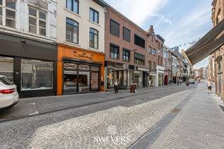 Voor meer info en foto’s, surf naar www.swevers.be – Op een centrale locatie aan de Stapelstraat 38 in Sint-Truiden bevindt zich dit instapklare handelshuis, ideaal voor ondernemers die op zoek zijn naar een commerciële uitvalsbasis met veel opslag- en werkruimte. Het pand beschikt over een bruikbare oppervlakte van 272 m² op een perceel van 1a 06ca en combineert de charme van een historisch gebouw met hedendaags comfort dankzij verschillende renovaties. Op het gelijkvloers bevindt zich de winkelruimte met achteraan een ruime keuken van 41,47 m², twee afzonderlijke koelcellen en een apart toilet. De eerste verdieping biedt een bureau, technische ruimte, berging en ongeveer 78 m² opslagruimte. Op de tweede verdieping is er nog een extra opslagplaats van circa 33 m², terwijl de ingerichte zolder van 26 m² bijkomende mogelijkheden biedt voor stockage of ondersteunende activiteiten. Het pand werd doorheen de jaren grondig vernieuwd. In 2000 werden onder meer de elektriciteit, gasinstallatie en winkelinrichting vernieuwd. In 2018 volgden een nieuw dak en de afwerking van de tweede verdieping en zolder. In 2023 werden 9 zonnepanelen geplaatst en het volledige gebouw uitgerust met energiezuinige ledverlichting. Er is een mogelijkheid tot overname van het handelsfonds voor 45.000 euro. De ligging is een grote troef: op slechts 500 meter van de Grote Markt, met winkels en restaurants op wandelafstand en een vlotte bereikbaarheid via openbaar vervoer en de snelwegen. Een uitstekende opportuniteit voor wie een instapklare commerciële eigendom zoekt op een toplocatie in Sint-Truiden. Voor meer informatie, bel 012 699 900. Bron bewoonbare oppervlakte: EPC – verslag.