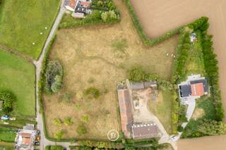 Aan de zuidflank van Wemmel, op de grens tussen stad en stilte, ligt een plek die nog ademt wat ooit was: het Ronkelhof. Verspreid over ruim één hectare glooiend landschap, vormt deze historische hoeve een zeldzaam relict van het landelijke leven rond Brussel.<br /><br />Het Ronkelhof gaat terug tot de 18de eeuw en was ooit deel van een middeleeuwse vierkantshoeve. Vandaag staat het als enige authentiek bewaarde pachthof in Wemmel, met zijn witgekalkte bakstenen gebouwen, gepikte plint en karakteristieke zadeldaken. De site is gelegen op een heuvel en bereikbaar via een holle weg, een schilderachtig toegangspad dat haast tijdloos aanvoelt.<br /><br />De gebouwen, vandaag niet meer bewoonbaar, wachten op een renovatie die hun historische waarde eer aandoet. Hier ligt een uitzonderlijke kans voor wie erfgoed een toekomst wil geven, in ruil voor rust, ruimte en een unieke locatie vlak bij de hoofdstad. De boomgaard achteraan herinnert aan het landleven van vroeger en vormt een stille belofte van eenvoud en natuur.