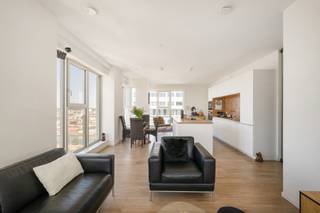 Op een unieke locatie aan het Kempisch Dok bevindt zich op de 22ste verdieping van de iconische Doktoren dit uitzonderlijke penthouse van ca. 132 m². Dankzij de ligging op de hoogste woonverdiepingen en de oriëntatie over drie zijden geniet u van indrukwekkende vergezichten, met als absolute blikvanger het frontale zicht over het Kempisch Dok en de Antwerpse skyline.
De inkomhal beschikt over een gastentoilet en geeft toegang tot de master bedroom met aangrenzend terras en elegante ensuite badkamer met lavabomeubel, inloopdouche en toilet. Daarnaast is er een praktische technische/wasruimte.
De lichtrijke leefruimte wordt gekenmerkt door kamerhoge beglazing en een open keuken die volledig geïnstalleerd is. Vanuit de leefruimte bereikt u het tweede terras, dat volledig met beglazing kan worden afgesloten en zo dienstdoet als aangenaam winterterras.
Aan de andere zijde bevinden zich twee bijkomende slaapkamers waarvan één momenteel als bureauruimte wordt gebruikt en ideaal is als home office. Een tweede badkamer met lavabomeubel en inloopdouche en een afzonderlijk toilet vervolledigen dit niveau.
Het appartement beschikt over vloerverwarming en privatieve zonnepanelen. Op de 23ste verdieping kunnen bewoners bovendien genieten van een gemeenschappelijk dakterras met een uniek panorama over Antwerpen en het omliggende waterlandschap.
Inclusief privatieve kelderberging. Een ondergrondse autostaanplaats dient verplicht bij aangekocht te worden voor € 40.000.
