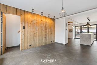 Voor meer info en foto’s, surf naar www.swevers.be – In het hart van Leopoldsburg vindt u deze charmante en instapklare rijwoning met centrale ligging in de Tramstraat. inkels, scholen, restaurants en openbaar vervoer liggen op wandelafstand, wat deze woning ideaal maakt voor eigen bewoning én als investering. De woning werd oorspronkelijk gebouwd in 1965, maar onderging de voorbije jaren belangrijke renovaties. Zo werden de voorgevelramen vernieuwd in 2012 en volgde in 2021 een totaalrenovatie van onder meer keuken, badkamer, elektriciteit, verwarming, dak en achtergevelramen. Met een bewoonbare oppervlakte van 152 m² is er verrassend veel ruimte. Op de eerste verdieping bevindt zich een gezellige leefruimte van 18,44 m², aansluitend op een ruime en moderne keuken van 17,13 m². Van hieruit heeft u rechtstreeks contact met het overdekte terras van 13 m². De glaspartij tussen keuken en terras kan volledig opengeschoven worden, waardoor binnen en buiten mooi in elkaar overlopen. Op de tweede verdieping zijn er twee slaapkamers, waaronder één met dressing. De tweede kamer van 13,92 m² is geschikt als slaapkamer, bureau of hobbyruimte. De vernieuwde badkamer is praktisch en comfortabel ingericht. Achteraan ligt een onderhoudsvriendelijke tuin van 96,29 m². Verder beschikt de woning over een inpandige garage van 20,16 m² met sectionale poort, plus praktische berg- en wasruimte op het gelijkvloers. Dankzij EPC-label B, conforme elektriciteit en de huidige verhuur via een sociaal verhuurkantoor aan €700 per maand is dit ook een interessante, zorgeloze investering. Voor meer informatie, bel 011 255 155. Bron bewoonbare oppervlakte: EPC – verslag.
