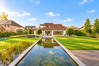 Op een bijzonder breed perceel van maar liefst 1.715 m² bevindt zich deze stijlvolle, hedendaagse woning van 322m²(bron EPC) waar architectuur, wooncomfort en buitenbeleving mooi samenvloeien. De ligging vormt daarbij een uitgesproken troef: de Kroonwinningstraat is een residentiële straat met een rechtstreekse aansluiting richting de Grote Ring, waardoor het centrum van Hasselt en de belangrijkste verbindingsassen vlot bereikbaar zijn.<br />De woning straalt een tijdloze, hedendaagse elegantie uit. Binnen zorgen royale raampartijen, open leefruimtes en de karaktervolle hoge plafonds met zichtbare dakstructuur voor een uitzonderlijk gevoel van ruimte en licht. Warme materialen, veel geïntegreerd maatwerk en een kwalitatief afwerkingsniveau geven het interieur een verfijnde maar tegelijk aangename en huiselijke uitstraling.<br />De leefruimtes staan sterk met elkaar in verbinding en kijken uit over de tuin. Wonen, tafelen en ontspannen vloeien natuurlijk in elkaar over, terwijl de openheid nergens ten koste gaat van gezelligheid. Het geheel werd duidelijk ontworpen met aandacht voor zichtlijnen, lichtinval en functionaliteit.<br />Met vier volwaardige slaapkamers en twee badkamers biedt de woning alle ruimte voor een gezin, zonder aan comfort of privacy in te boeten. Ook praktisch scoort het pand bijzonder sterk, onder meer dankzij de dubbele inpandige garage en de royale perceeloppervlakte.<br />Buiten wordt de architectuur doorgetrokken in een indrukwekkende, volledig aangelegde en inmiddels volwassen tuin. Strakke hagen, volwassen beplanting, ruime gazons en zorgvuldig gekozen terrassen creëren verschillende buitenkamers en zorgen tegelijk voor een bijzonder groen kader. Centraal in het tuinontwerp vormt de langgerekte zwemvijver een echte blikvanger. Het water, de beplanting en de open gazons versterken het gevoel van rust en ruimte dat op een perceel van deze omvang zo uitzonderlijk is nabij Hasselt.<br />Ook de omgeving draagt bij aan het bijzondere karakter van de locatie. In de Kroonwinningstraat bevindt zich het historische park De Kroonwinning, een landschappelijk park met grasveld, vijver en een waardevol bomenbestand. Inventaris Onroerend Erfgoed Tegelijkertijd blijft de stedelijke bereikbaarheid uitstekend: de straat sluit aan op de Gouverneur Roppesingel/Grote Ring en bevindt zich daarmee strategisch ten opzichte van Hasselt en de omliggende regio. Wegen en Verkeer<br />Kroonwinningstraat 72 is dan ook een woning voor wie niet wil kiezen tussen ruimte en bereikbaarheid, tussen architectuur en gezelligheid, of tussen stad en groen. Een uitzonderlijk breed perceel, een volwassen tuin met zwemvijver, vier slaapkamers, twee badkamers, een dubbele inpandige garage en een lichtrijk interieur met hoogwaardig maatwerk maken hiervan een bijzonder compleet woonverhaal op een gegeerde Hasseltse locatie.