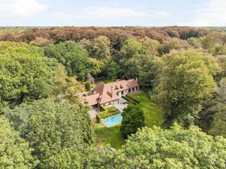Verscholen in het groen van de gegeerde Bellevuedreef bevindt zich deze karaktervolle klassieke villa op een indrukwekkend parkdomein van ca. 1,4 hectare. Een eigendom waar ruimte, privacy en een bijzonder aangename woonbeleving samenkomen, omgeven door een volgroeide en zorgvuldig aangelegde tuin.<br /><br />De villa beschikt over ca. 575 m² bewoonbare oppervlakte en wordt aangevuld met een volwaardig gastenverblijf in het poolhouse, een afzonderlijke conciërgewoning, een inpandige garage voor drie wagens en een verwarmd buitenzwembad. De omvang van het domein, de volwassen begroeiing en de verschillende woon- en verblijfsfuncties maken van deze eigendom een bijzonder compleet geheel op een van de meest residentiële locaties van Schilde.<br /><br />Indeling gelijkvloers:<br />De centrale inkomhal met vestiaire en gastentoilet vormt het vertrekpunt van de woning en geeft toegang tot de verschillende leefruimtes.<br />De royale leefruimte omvat een zitkamer en eetkamer, aansluitend op een afzonderlijke studeerkamer. Daarnaast bevindt zich een ruim bureel met maatwerkkasten, waardoor ook professioneel of rustig thuiswerken perfect in de woning kan worden geïntegreerd.<br />Centraal in het dagelijkse leven staat de ruime leefkeuken, opgebouwd rond een gezellige ontbijtruimte met grote schuiframen naar het terras en de tuin. Het keukengedeelte met eiland is uitgerust met diverse inbouwtoestellen. Een praktische berging zorgt voor een tweede verbinding met de eetkamer, terwijl de bijkeuken met afzonderlijke zij-ingang bijkomende functionaliteit biedt.<br /><br />Eerste verdieping:<br />De nachthal leidt naar vier ruime slaapkamers, die elk over een eigen badkamer beschikken.<br />De mastersuite vormt een royaal privégedeelte met slaapkamer, dressing en badkamer. Daarnaast bevinden zich op deze verdieping een tweede ruime slaapkamer, een gastenkamer en een kinderkamer, telkens met een eigen badkamer.<br /><br />Vanuit de mastersuite is er via een tussengang en diensttrap verbinding met het gedeelte boven de garage.<br /><br />Conciërgewoning:<br />Boven de inpandige garage bevindt zich een afzonderlijk verblijfs- en conciërgegedeelte, bestaande uit een polyvalente leefruimte, slaapkamer en badkamer. Dit gedeelte leent zich uitstekend voor inwonend personeel, een au pair, familie of gasten.<br /><br />Kelder:<br />Via een natuurstenen trap is de kelderverdieping bereikbaar. Hier bevinden zich bijkomende bergruimtes, de technische installaties voor de woning en het zwembad en een sfeervolle wijnkelder.<br /><br />Poolhouse &amp; gastenverblijf:<br />Aan het verwarmde zwembad bevindt zich een royaal bijgebouw, architecturaal afgestemd op de hoofdwoning. Het poolhouse werd ingericht als een volwaardig zelfstandig gastenverblijf met woonkamer, keuken, slaapkamer en badkamer.<br />Samen met de omliggende terrassen en het zwembad ontstaat hier een bijzonder aangename omgeving voor ontspanning, familie en gasten, met een grote mate van privacy ten opzichte van de hoofdwoning.<br /><br />Bijzonderheden:<br />- Uitzonderlijk parkdomein van ca. 14.433 m²<br />- Volledig omheind domein met maximale privacy<br />- Volgroeide tuin met uitgestrekte gazons en volwassen bomen<br />- Regelmatig onderhouden en verder opgefrist<br />- Verwarmd buitenzwembad<br />- Volwaardig poolhouse ingericht als zelfstandig gastenverblijf<br />- Afzonderlijk conciërge- of personeelsverblijf<br />- Inpandige garage voor drie wagens<br />- Verschillende ruime terrassen rondom de woning<br />- Uitgebreide tuinverlichting<br />- Alarm- en camerabewaking<br /><br />Een bijzonder compleet residentieel domein waar ruimte, discretie en groen centraal staan, op een van de meest gewaardeerde locaties van Schilde.