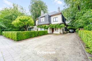 Maak kennis met deze karaktervolle doch op te frissen villa van 1939 ontworpen door architect H. Verbruggen, opgebouwd in de interbellumstijl, en gelegen op een ruim perceel aan de rand van een gegeerde villawijk in Sint-Kruis vlakbij scholen, winkels, station, ziekenhuis, centrum Brugge, ontspaningsmogelijkheden,... <br />De unieke en authentieke uitstraling van de villa gecombineerd met de groene omgeving maakt deze woonst dan ook erg bijzonder. <br /><br />De villa werd door de huidige eigenaars in 1990 uitgebreid tot een woning met praktijkgedeelte (die perfect kan dienen als bureel of kangoeroewoning). Dit praktijk/kangoeroegedeelte heeft een afzonderlijke praktische ingang. <br />De hoofdwoning dient op bepaalde aspecten wel terug gemoderniseerd te worden om terug aan het hedendaags wooncomfort te kunnen voldoen. <br /><br />De villa betreden we via een statige en ruime inkomhal met authentieke trap. Verder begeven we ons naar de riante leefruimte opgesplitst in verschillende zithoeken die van elkaar afgescheiden zijn via authentieke boogstructuren, een naastgelegen afzonderlijke eetplaats en keuken. <br />Voorts vinden we op de gelijkvloerse verdieping nog een doorgang terug naar het bijgebouwde praktijk/bureelgedeelte. Daar vinden we nog een apart toilet terug, kitchenette, douchekamer en een leefruimte/bureelruimte of ruimte die kan dienen als extra leefruimte/kangoeroewoning. <br /><br />Op de eerste verdieping vinden we 4 slaapkamers terug (waarvan masterbedroom met annex dressing/bureau) en een badkamer. <br />Op de tweede (zolder)verdieping vinden we nog een 5e slaapkamer of polyvalente kamer terug die te bereiken is via een vaste trap. <br /><br />Deze villa beschikt naast de riante achtertuin tevens over een mooi aangelegde voortuin met afzonderlijke toegang tot het praktijk/bureelgedeelte, alsook een parking voor wagens en oprit naar achteren met carport.<br /><br />Kortom: een zeldzame en ruime villa gelegen op een uiterst gegeerde en strategische locatie. Contacteer ons snel voor een bezoek aan dit eigendom via info@delbecque.immo of 050 45 03 45