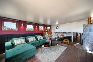 Bekijk deze boot uitgebreid op www.koosi.beDeze prachtige woonboot ‘Ons Genoegen’ is een blikken klipper van 1893 die ooit gebouwd is om steenkool te vervoeren over het water. De boot is gelegen op de mooiste plaats aan het Houtdok-Zuidkaai, de instapprijs van de concessie is inbegrepen in de koopsom. De romp is gemaakt uit staal van 6 mm dik en is de laatste keer officieel gecontroleerd in oktober 2024. Via de aanlegsteiger betreden we de boot en komen we op het achterdek waar de stuurinrichting van de boot is geplaatst. Als we dan binnenkomen in de leefruimte voelen we direct de gezelligheid die deze woonboot kan bieden, zeker door de aanwezigheid van de speksteenkachel. Deze ruimte is zeer groot en door de leuke lichtinval wordt dit nog eens extra benadrukt. Op het hogere deel is momenteel het salon geplaatst vanwaar je door de vele ramen direct zicht hebt op het water. Als we dan een paar trappen naar beneden lopen komen we in het gedeelte waarin de zeer ruime en volledig ingerichte keuken is gebouwd. Aan de andere kant vinden we de grote eettafel en toegang tot de ‘kelderruimte’. In voorste deel van boot zijn de slaapvertrekken voorzien. Vanuit de leefruimte komen we in een gang met rechts een berging waar wasmachine en droogkast kunnen geplaatst worden. Aan de overzijde van deze berging vinden we de technische ruimte met verwarmingsketel en pompen. Naast deze technische ruimte is het toilet gelegen. Iets verder in de gang vinden we rechts (stuurboordzijde) een slaapkamer met dubbel bed. Over deze slaapkamer (bakboordzijde) is de eerste badkamer met douche voorzien. Nog iets verder rechts is dan de 2de slaapkamer voorzien, deze kamer is momenteel ingericht als dressing en heeft een enkel bed. Over deze slaapkamer ligt de 2de badkamer, ook voorzien met lavabo en douche. Helemaal vooraan de boot komen we in de grote slaapkamer met ingebouwde kasten.